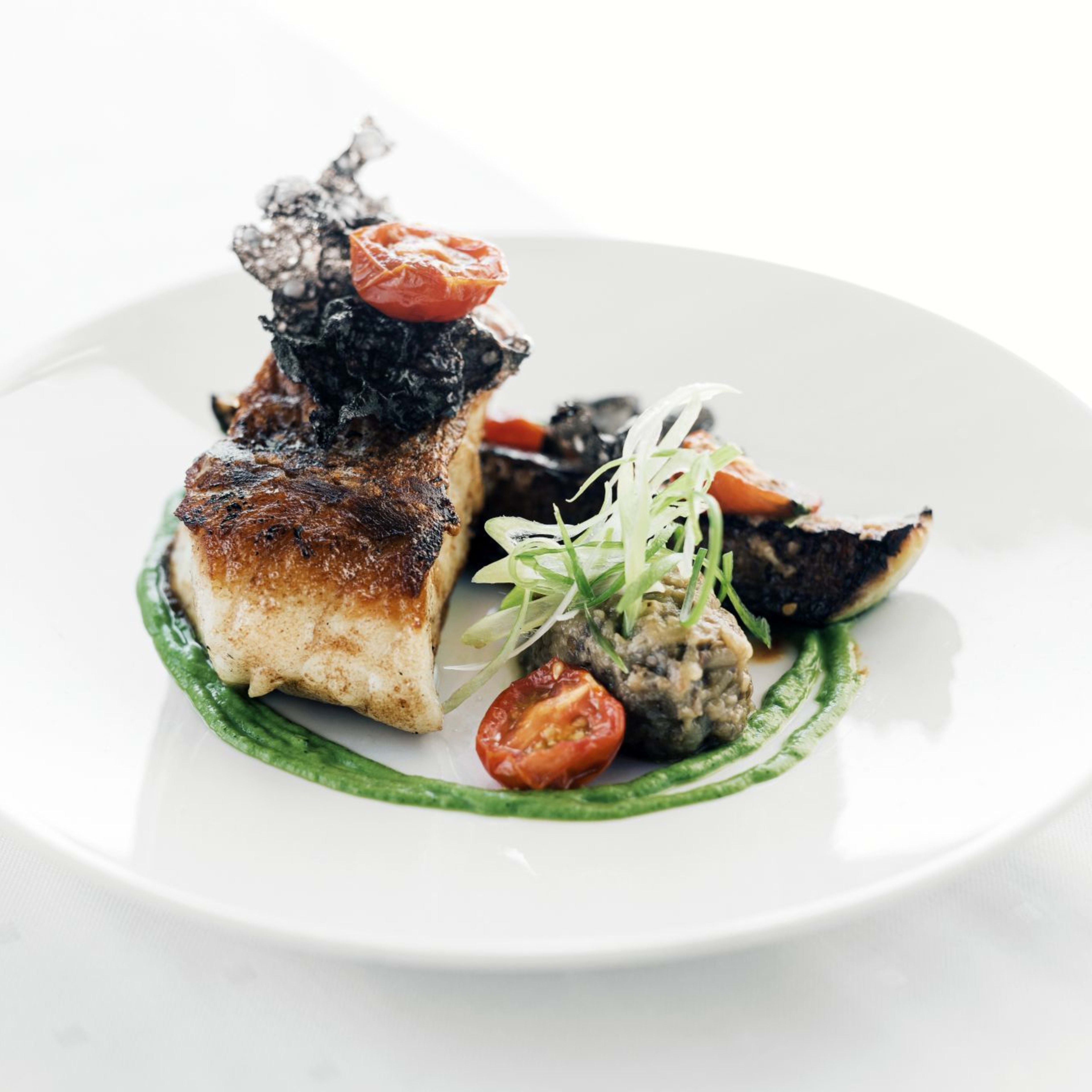 Gourmet dish of seared fish with golden crust, vibrant puree, crispy garnish, and roasted vegetables.