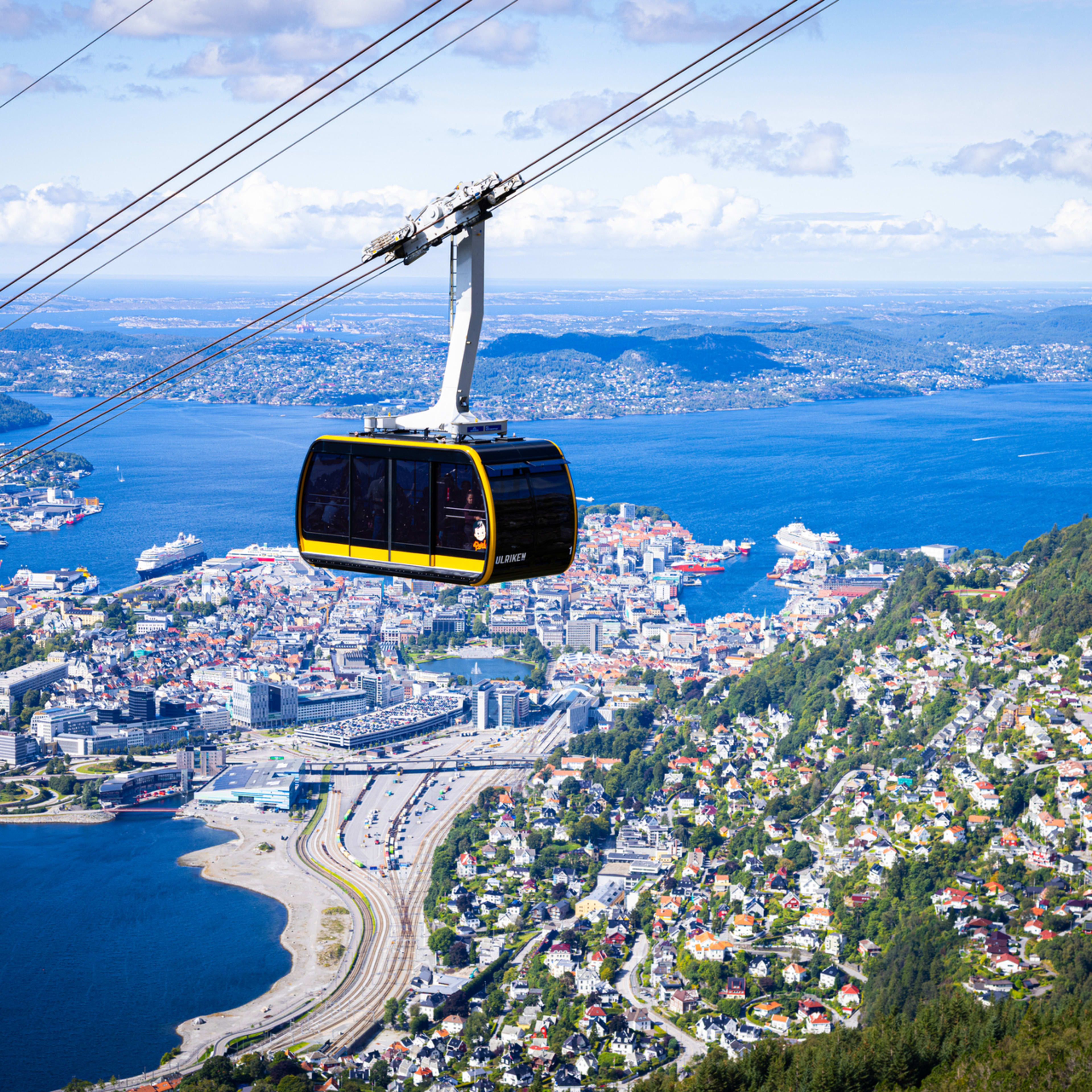 Yellow Ulriken cable car ascending to mountain top restaurant in Bergen with fjord and city views below