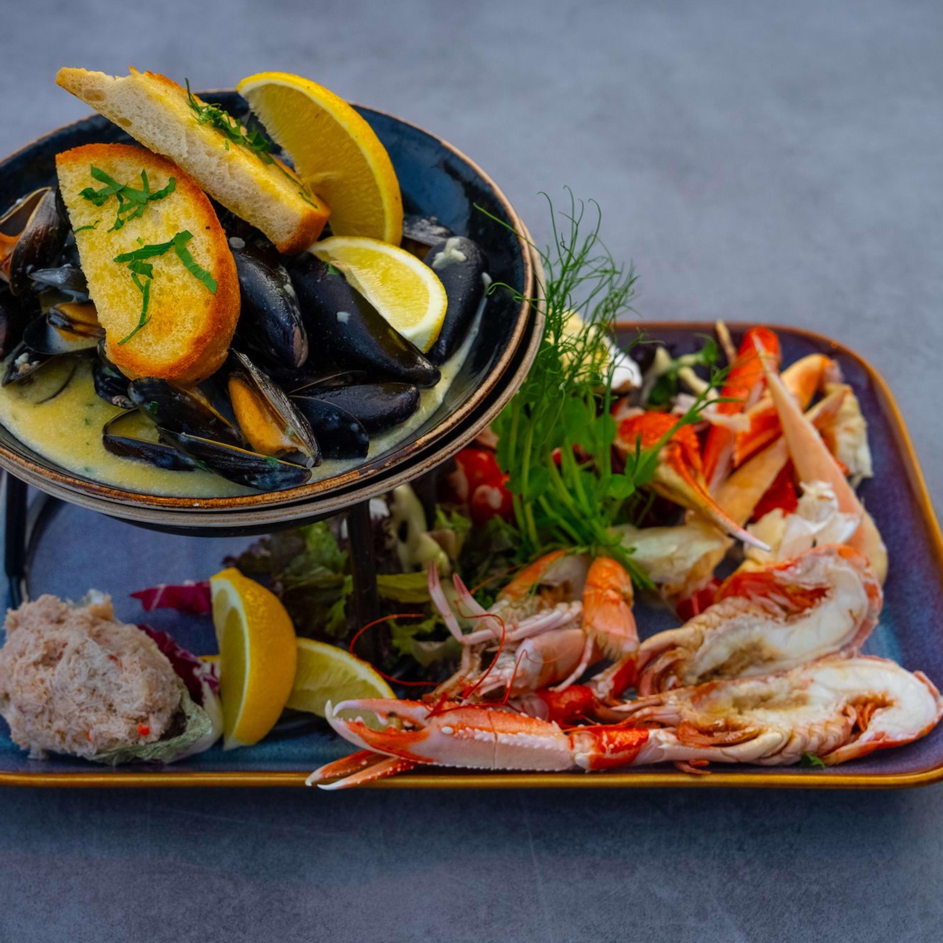 Eine luxuriöse Meeresfrüchteplatte mit Muscheln, Hummer, Garnelen, Krabbenbeinen und einem cremigen Meeresfrüchtespread auf einem zweistufigen Ständer.