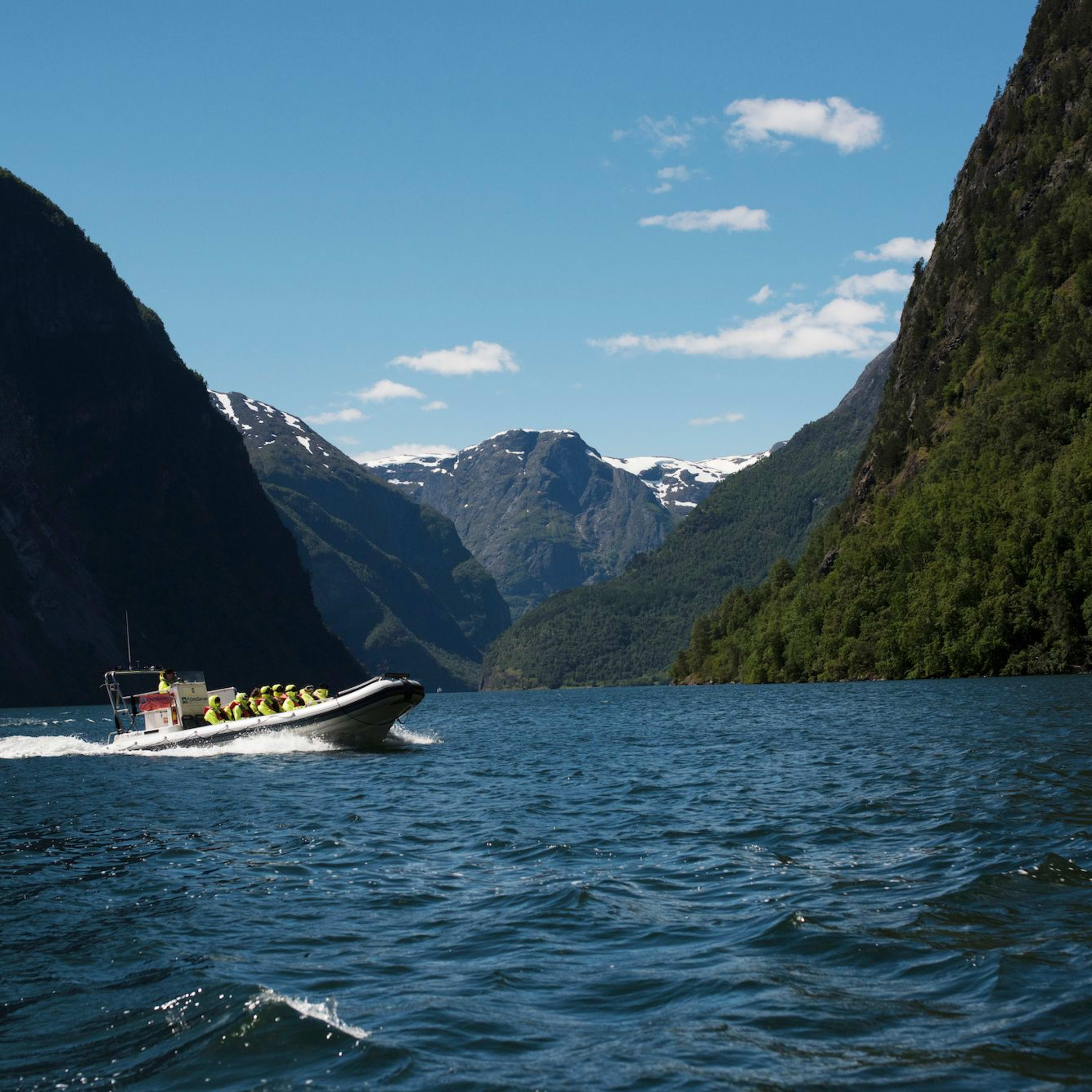 Hochgeschwindigkeits-Boot mit Passagieren in Rettungswesten fährt durch einen Fjord mit schneebedeckten Bergen.