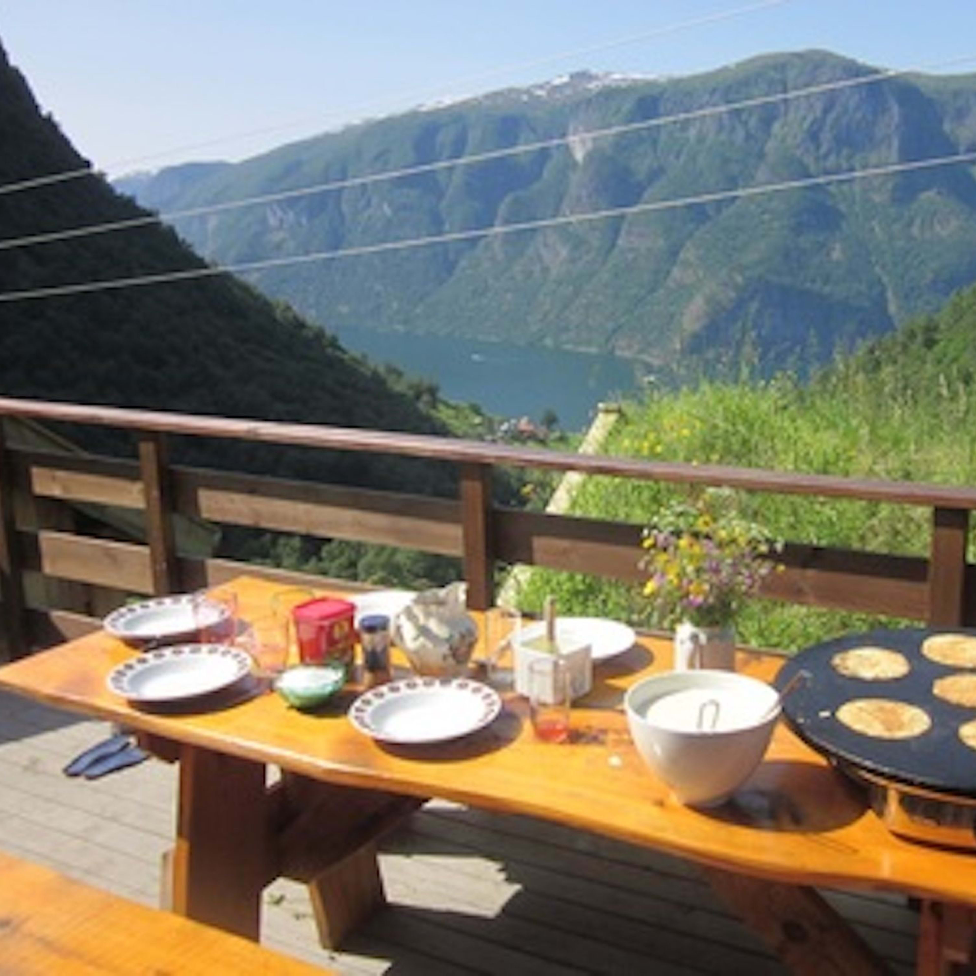 Rustikaler Tisch im Freien mit Tellern, Gewürzen, Teigschüssel und Pfannkuchen, mit Bergblick.