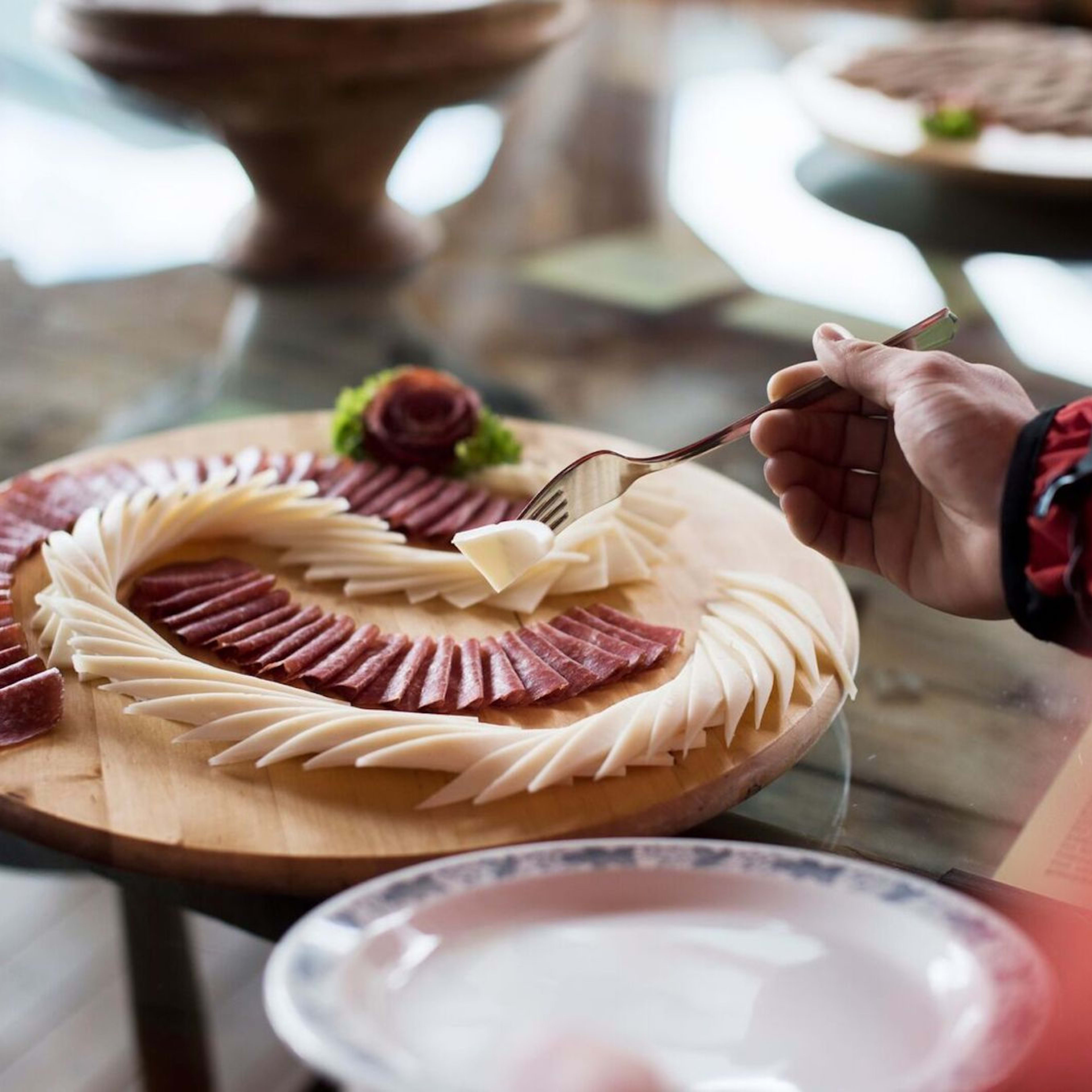 Trebrett med hvitost og spekemat arrangert i elegante kurver, pyntet med salat og roseformet kjøtt.