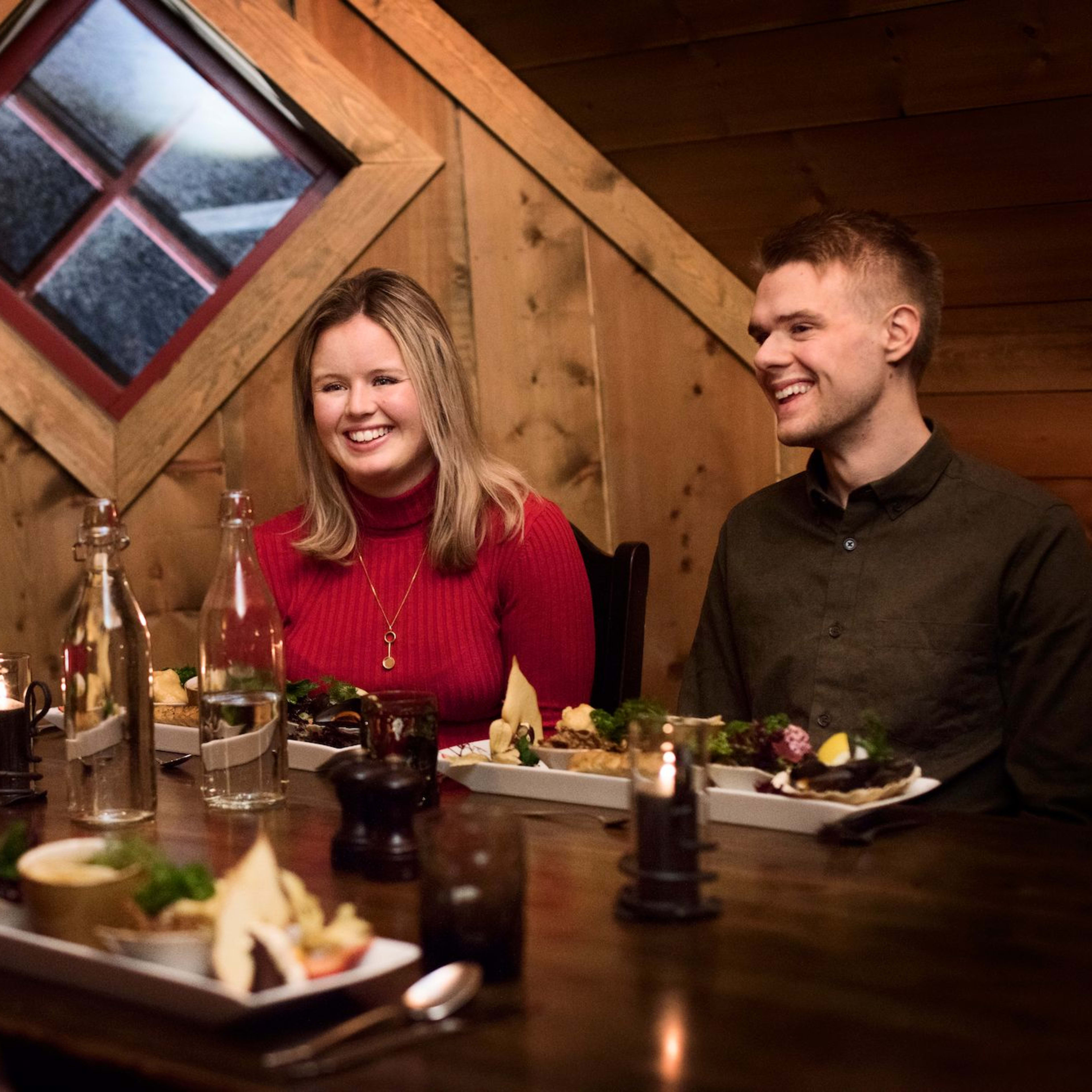 Freunde genießen ein gemütliches Abendessen in einer rustikalen Holzhütte mit Tellern mit Essen, Kerzen und einladender Atmosphäre.