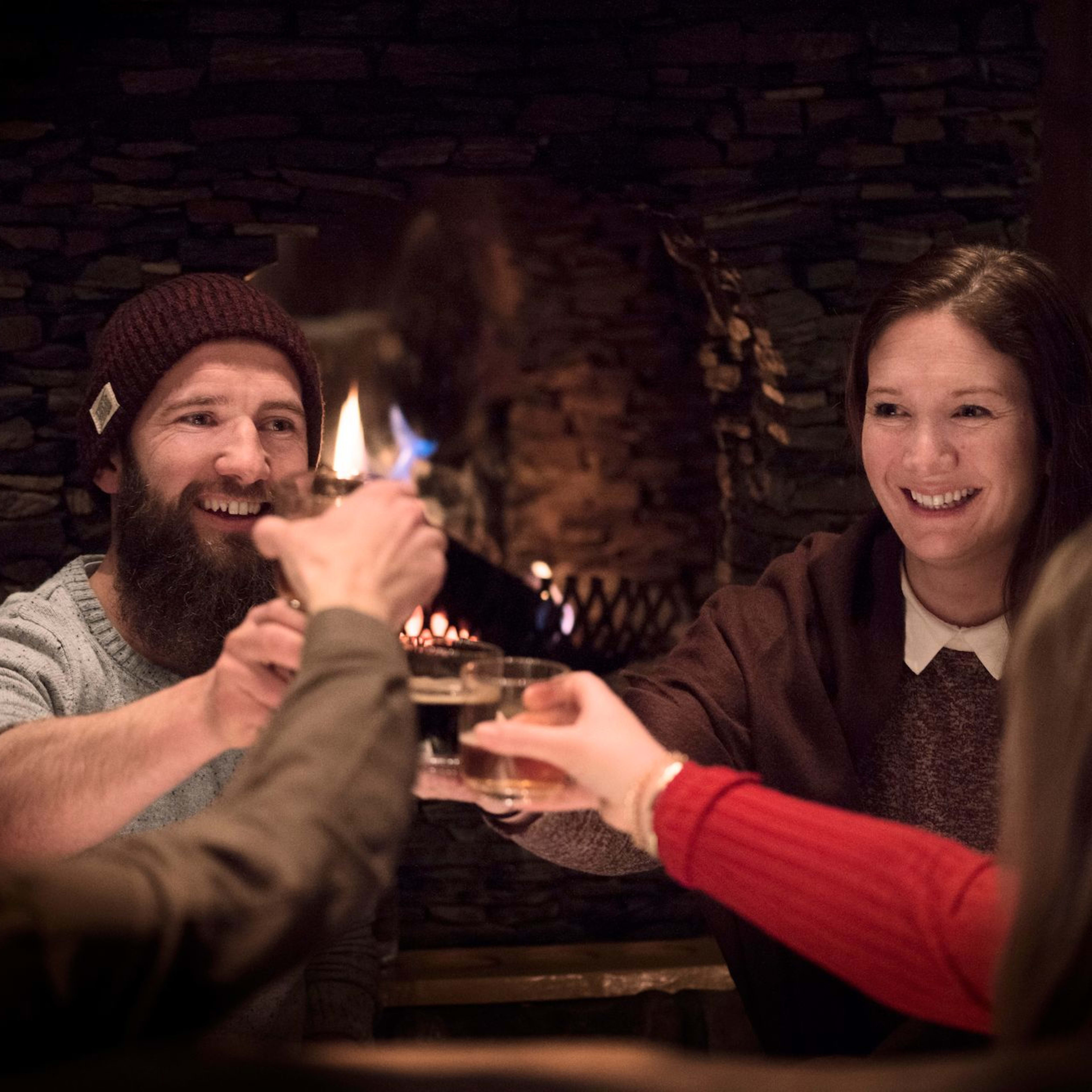 Venner samlet rundt en koselig steinpeis, hever glassene i en gledelig skål, og skaper en varm og glad atmosfære.