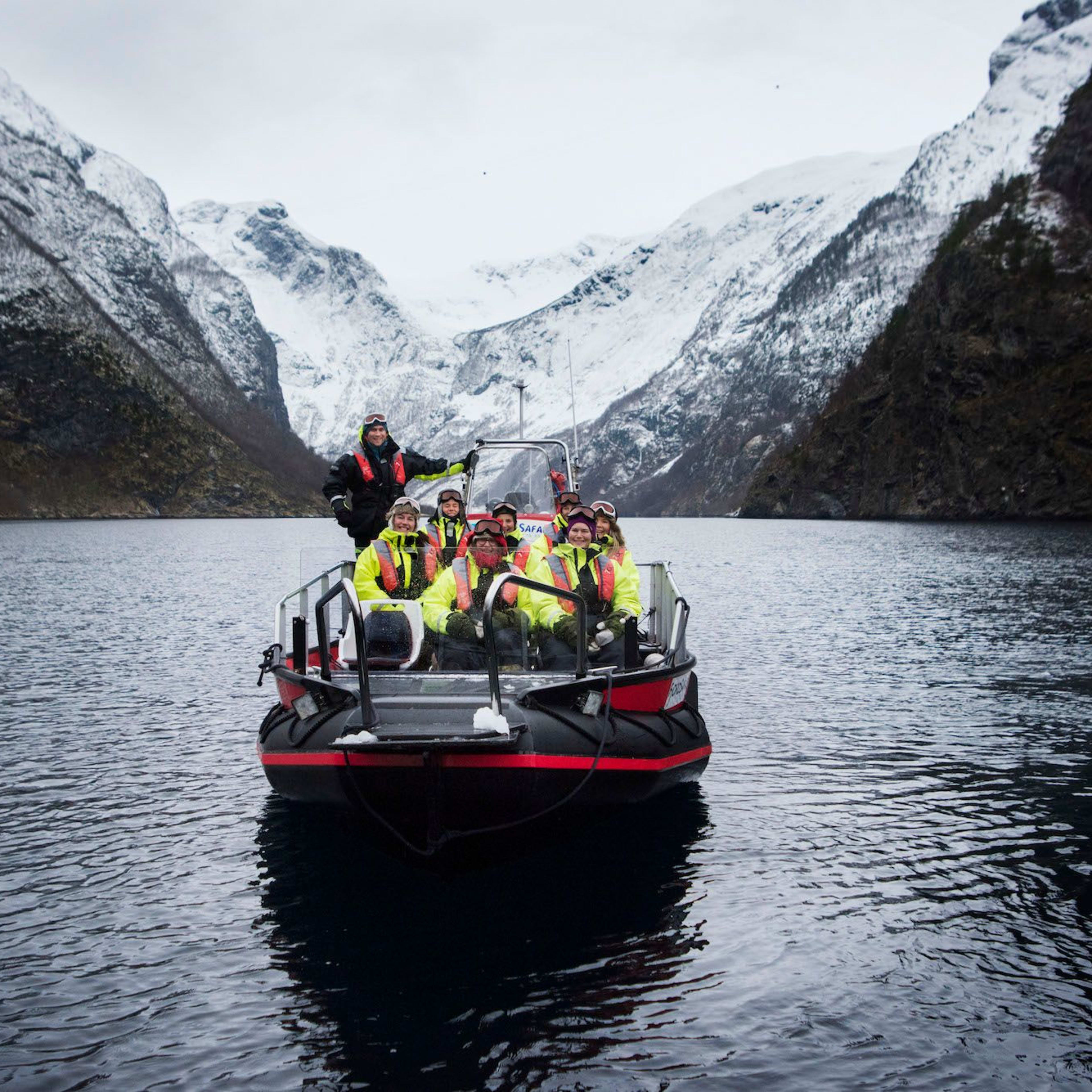 Menschen in leuchtend gelben Thermokombinationen auf einem Boot, lächelnd und posierend für ein Foto auf ruhigem Fjordwasser.