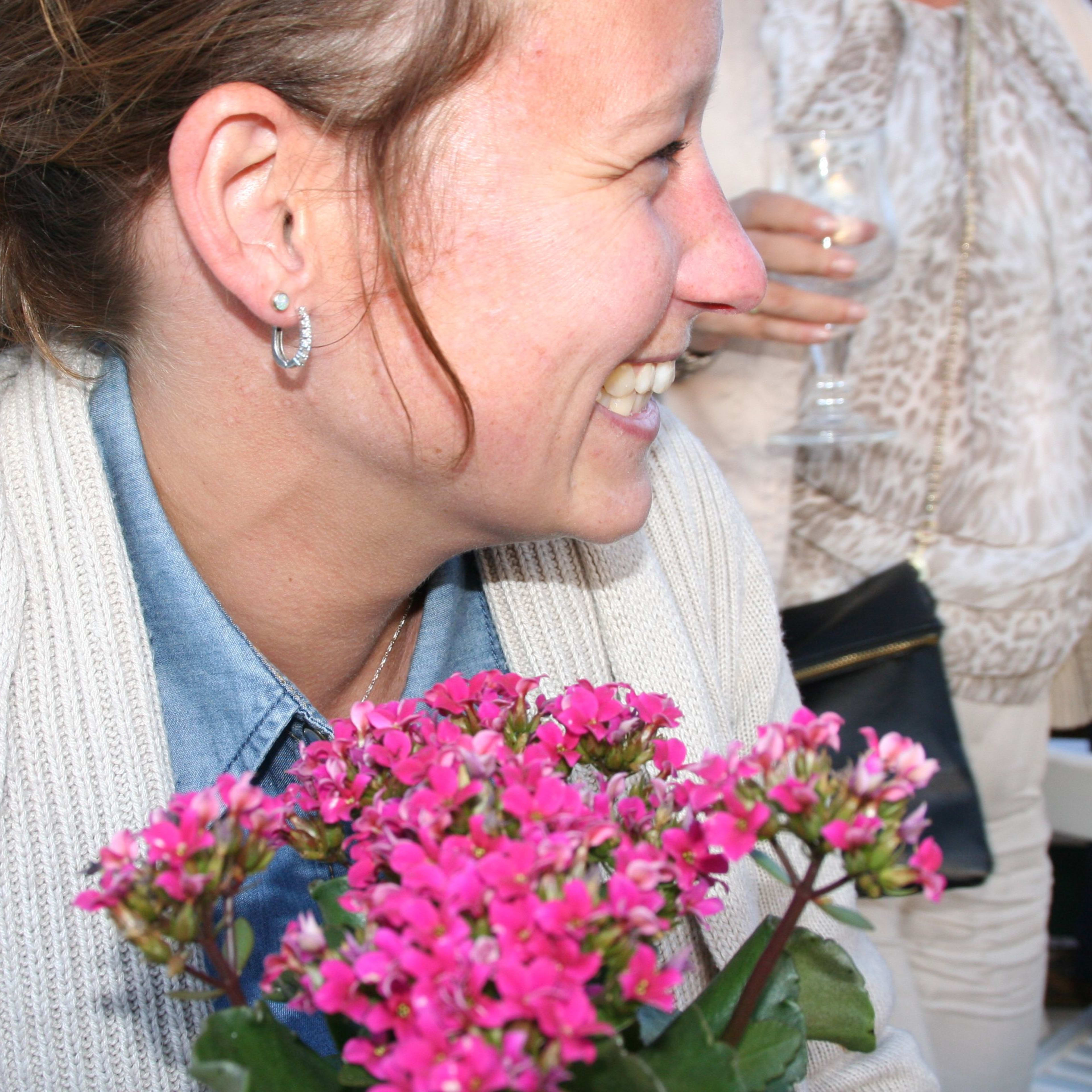 Joyful woman smiling brightly while holding a bouquet of pink flowers, dressed in cozy cardigan and denim shirt.