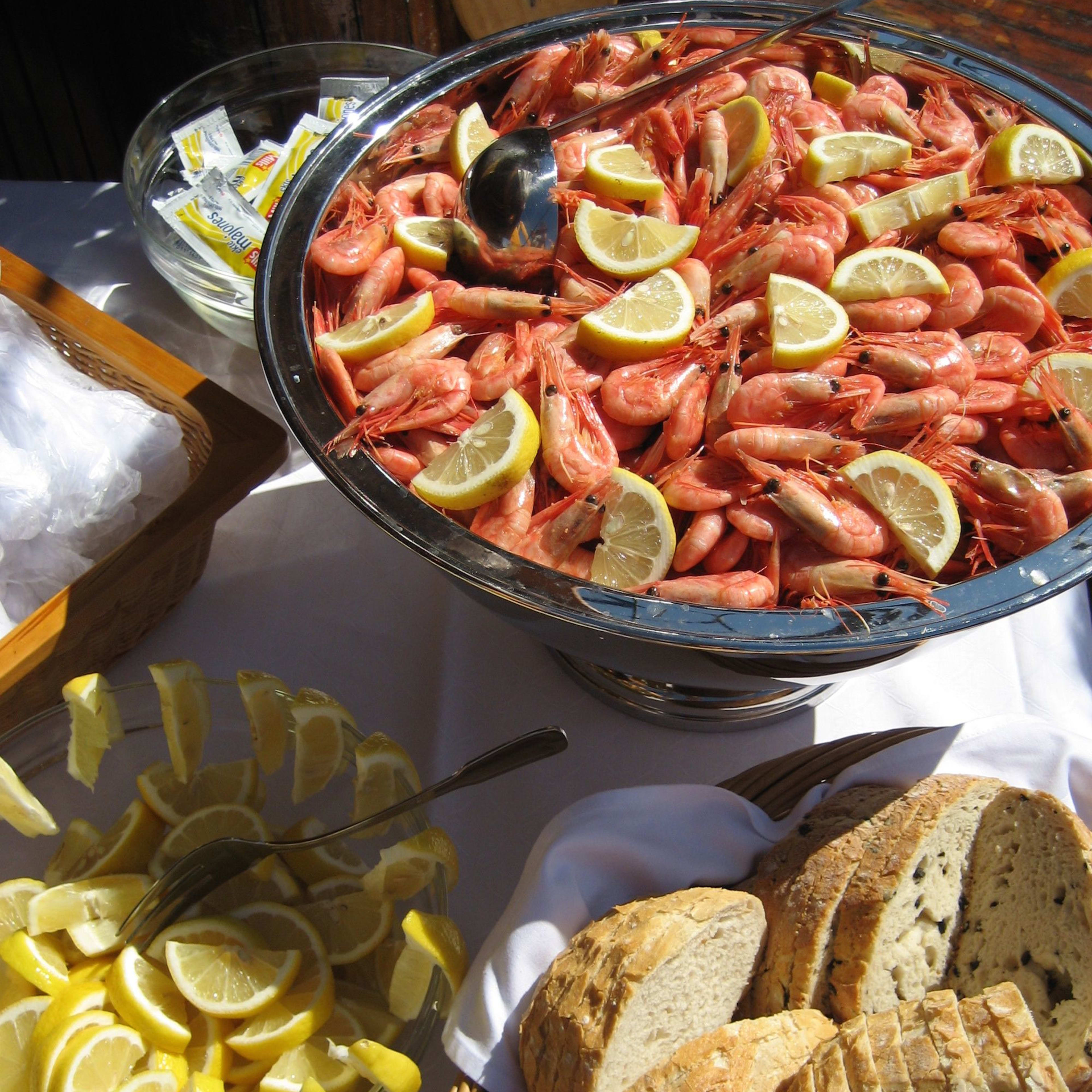 Lavish seafood buffet with shrimp, bread, lemon slices, and condiments, surrounded by vibrant sunlight.