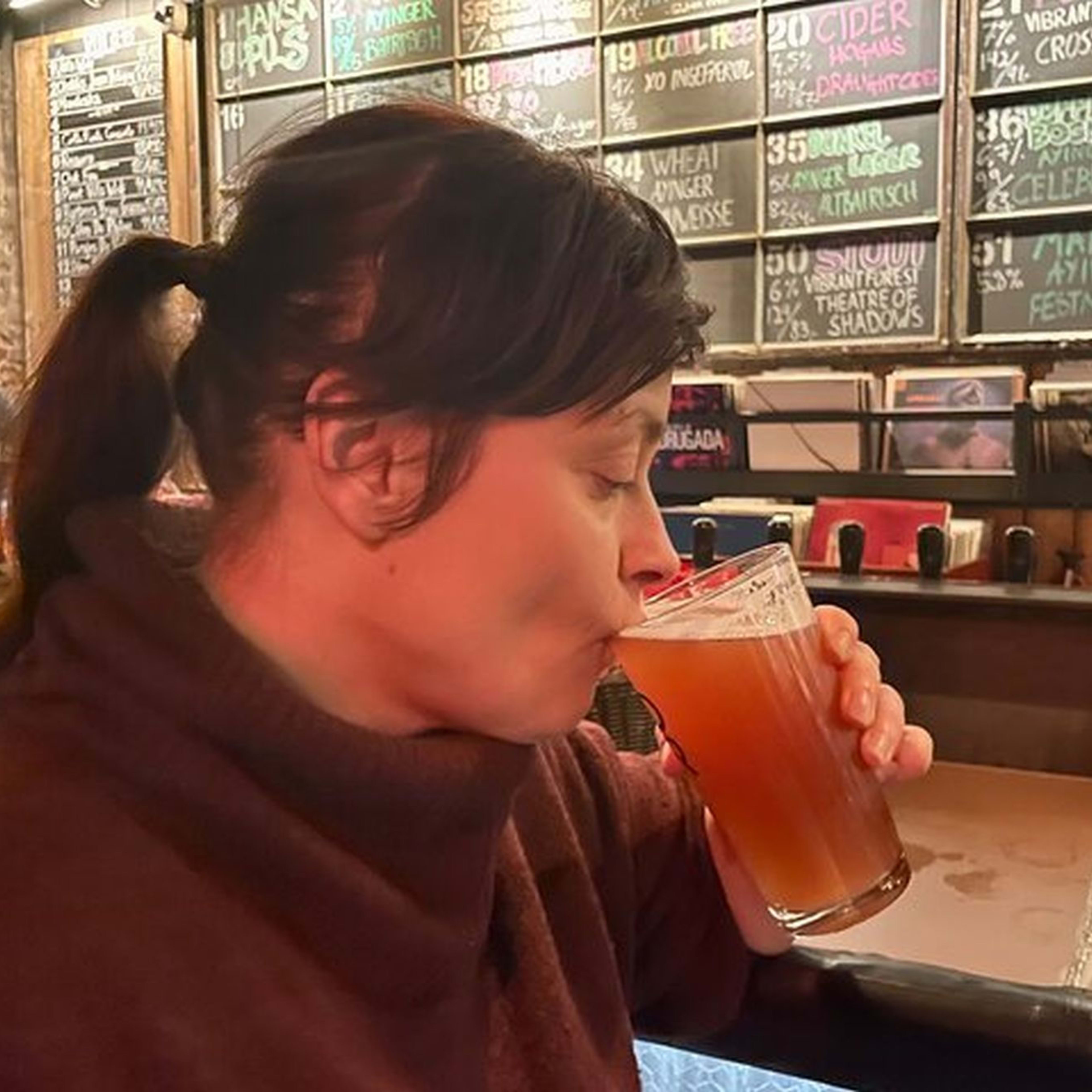 Kvinne som nyter amber håndverksøl på koselig bar, nyter smaken med lukkede øyne, varm belysning og rustikk innredning i bakgrunnen.