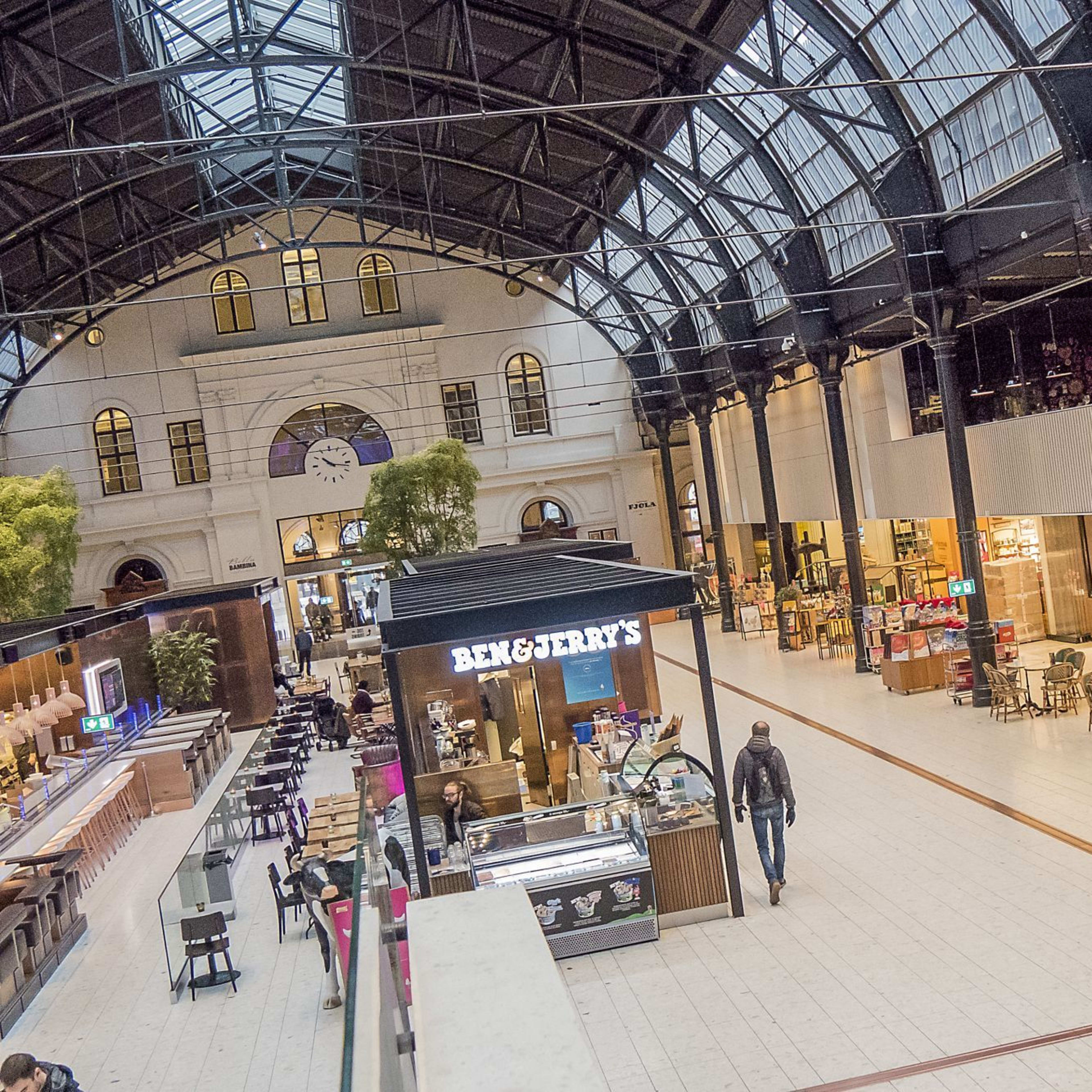 En moderne innendørs shoppinghall med høyt tak, matutsalg og naturlig lys som flommer inn i rommet.