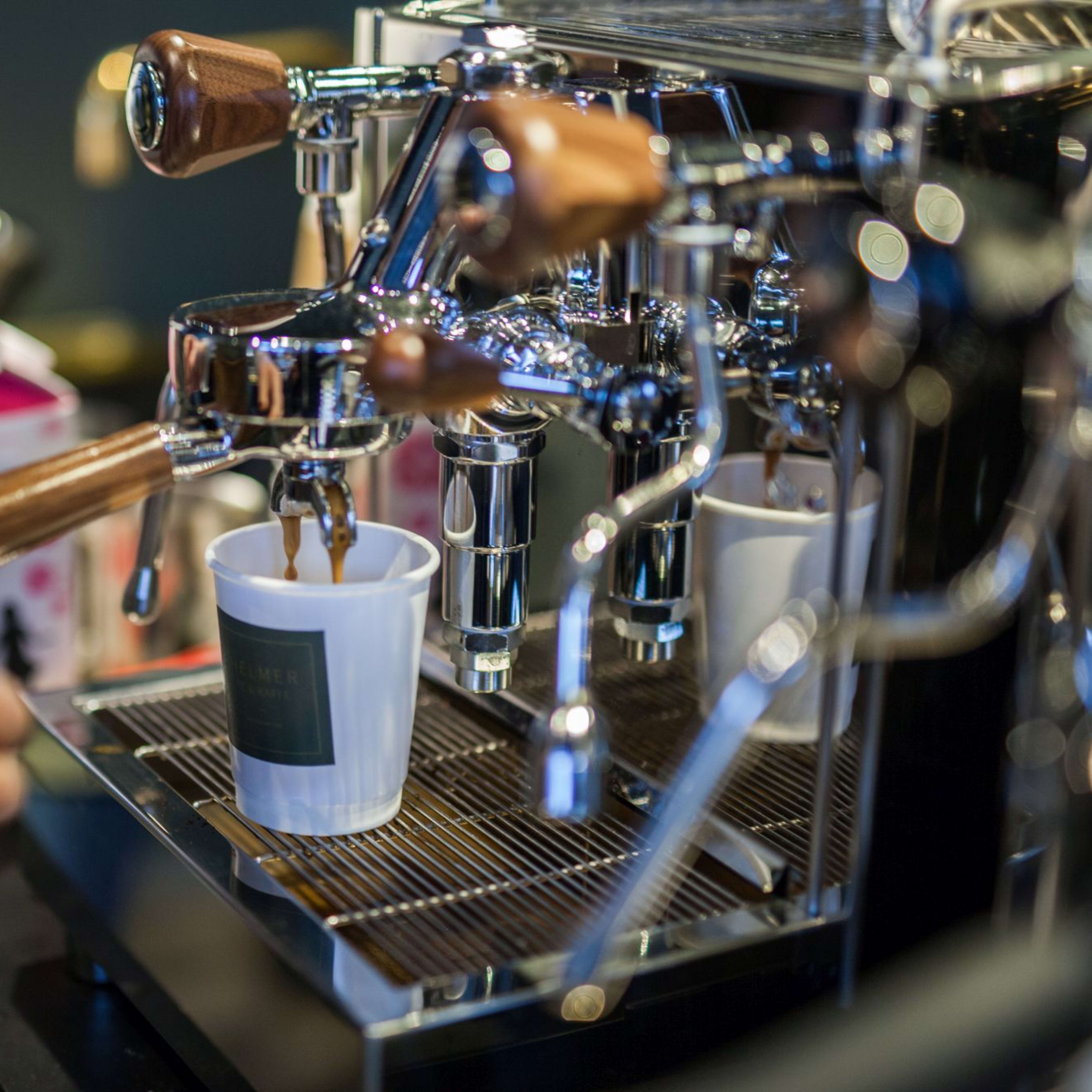 En høykvalitets espressomaskin med trekkerhåndtak som leverer fersk espresso i en papirkopp.