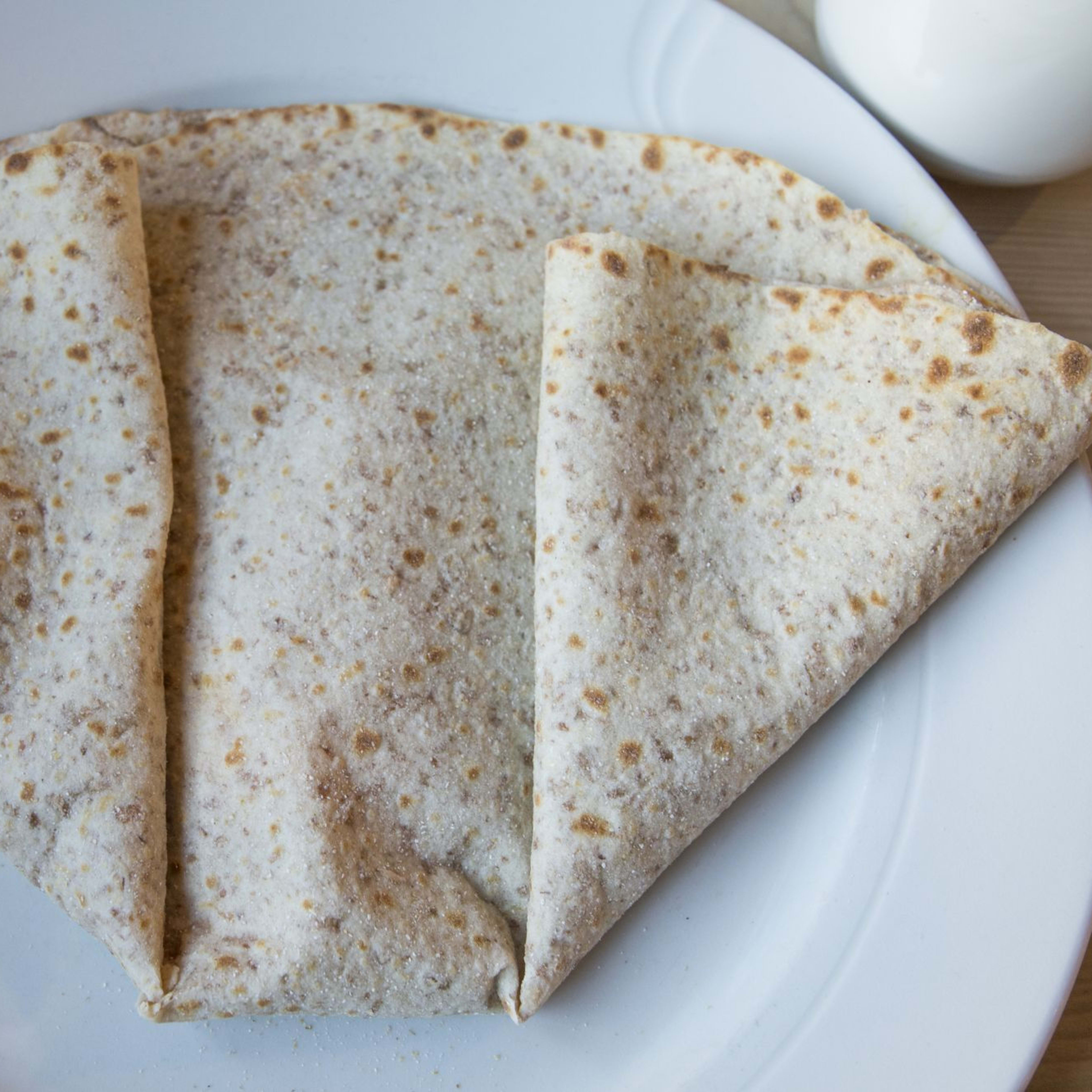 Ein gefaltetes Lefse, ein traditionelles norwegisches Fladenbrot, serviert auf einem weißen Teller mit rustikalem Hintergrund.