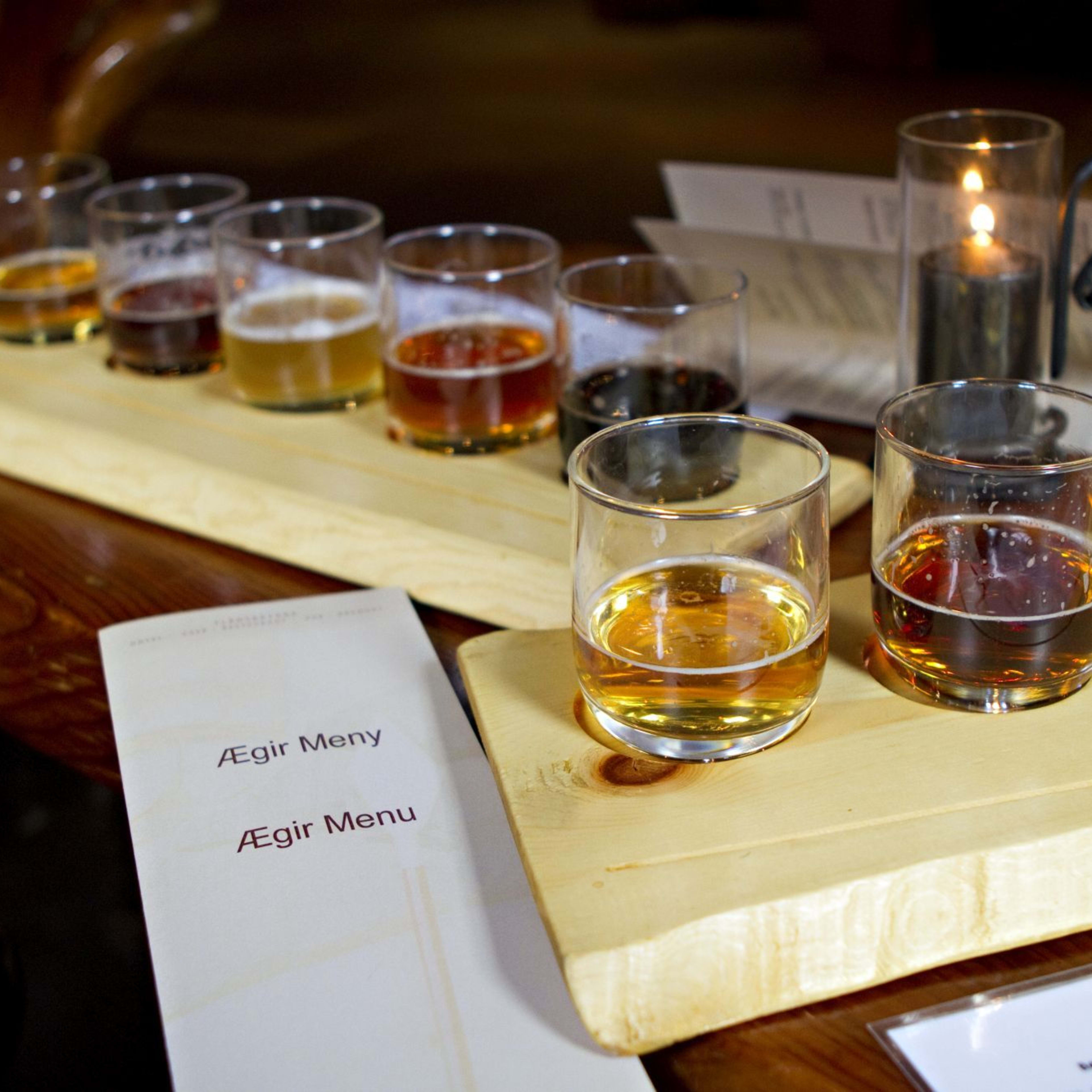 Holzflugbrett mit kleinen Cidergläsern, Kerze und "Ægir Meny"-Menü, was auf eine Cider-Verkostungserfahrung hinweist.