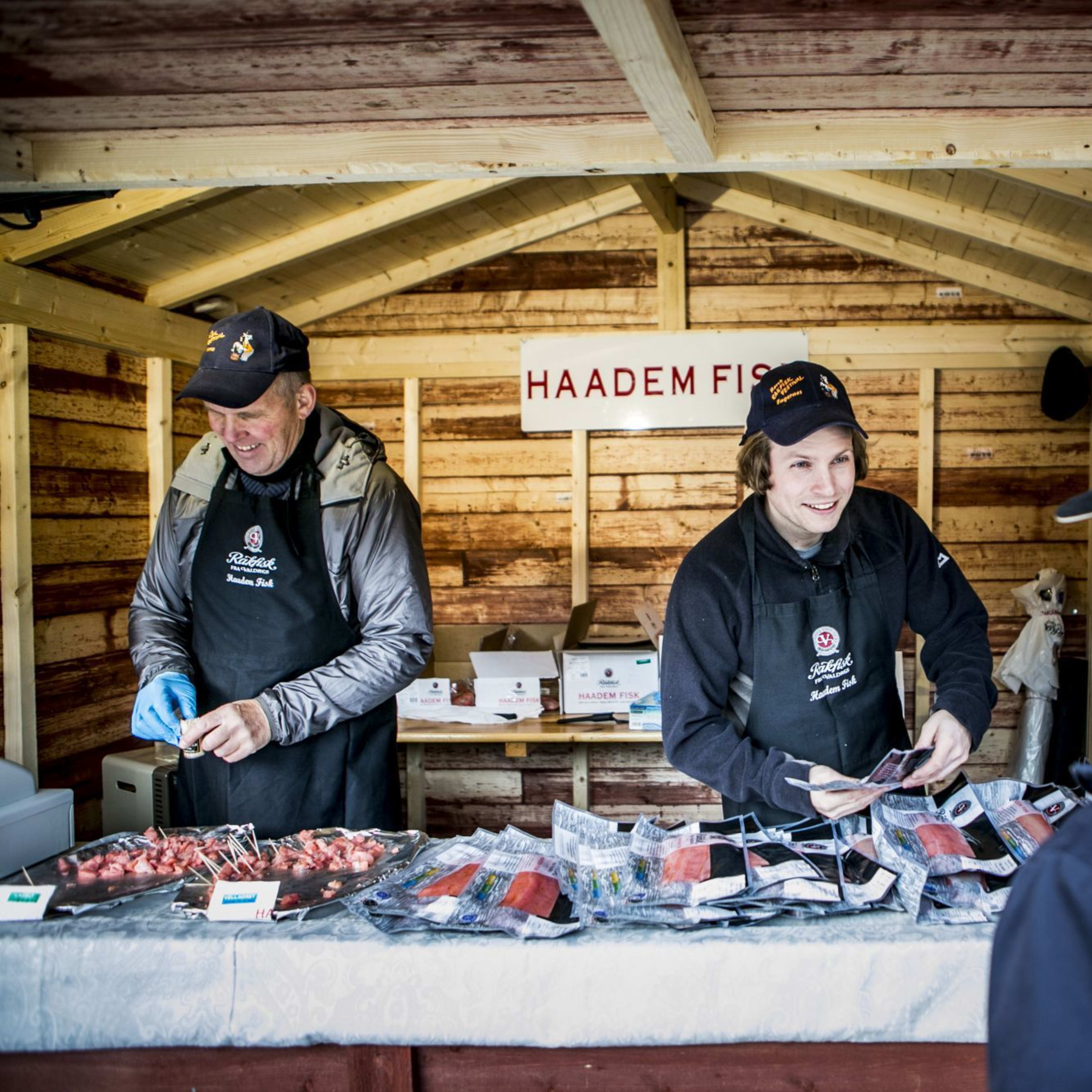 Markedsbod "Haadem Fish" med selgere som interagerer med kunder, rustikk treinteriør og fersk fisk til salgs.