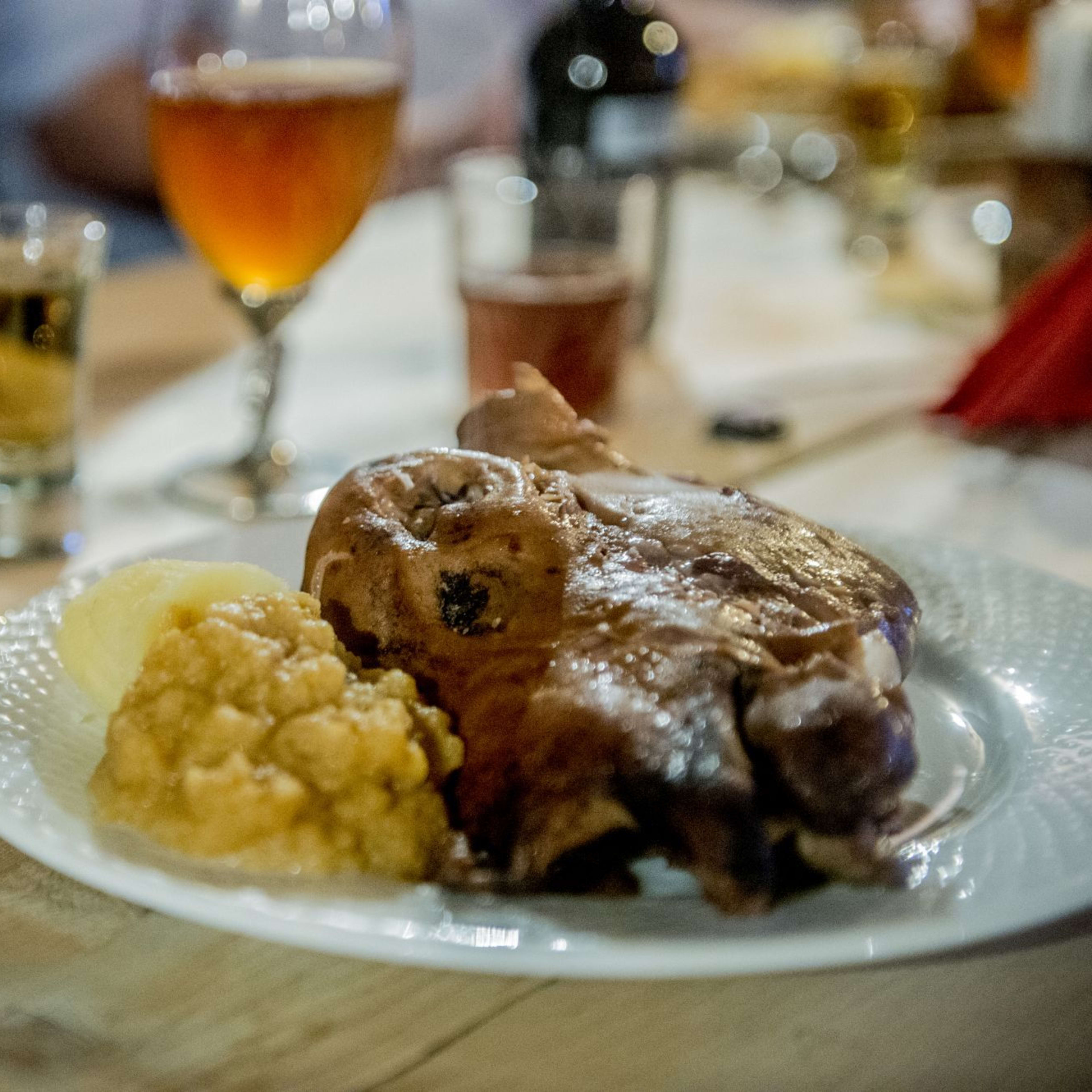 TraditionalSmalahove form Voss e with potatoes and yellow sauce on rustic wooden table, drinks in background.