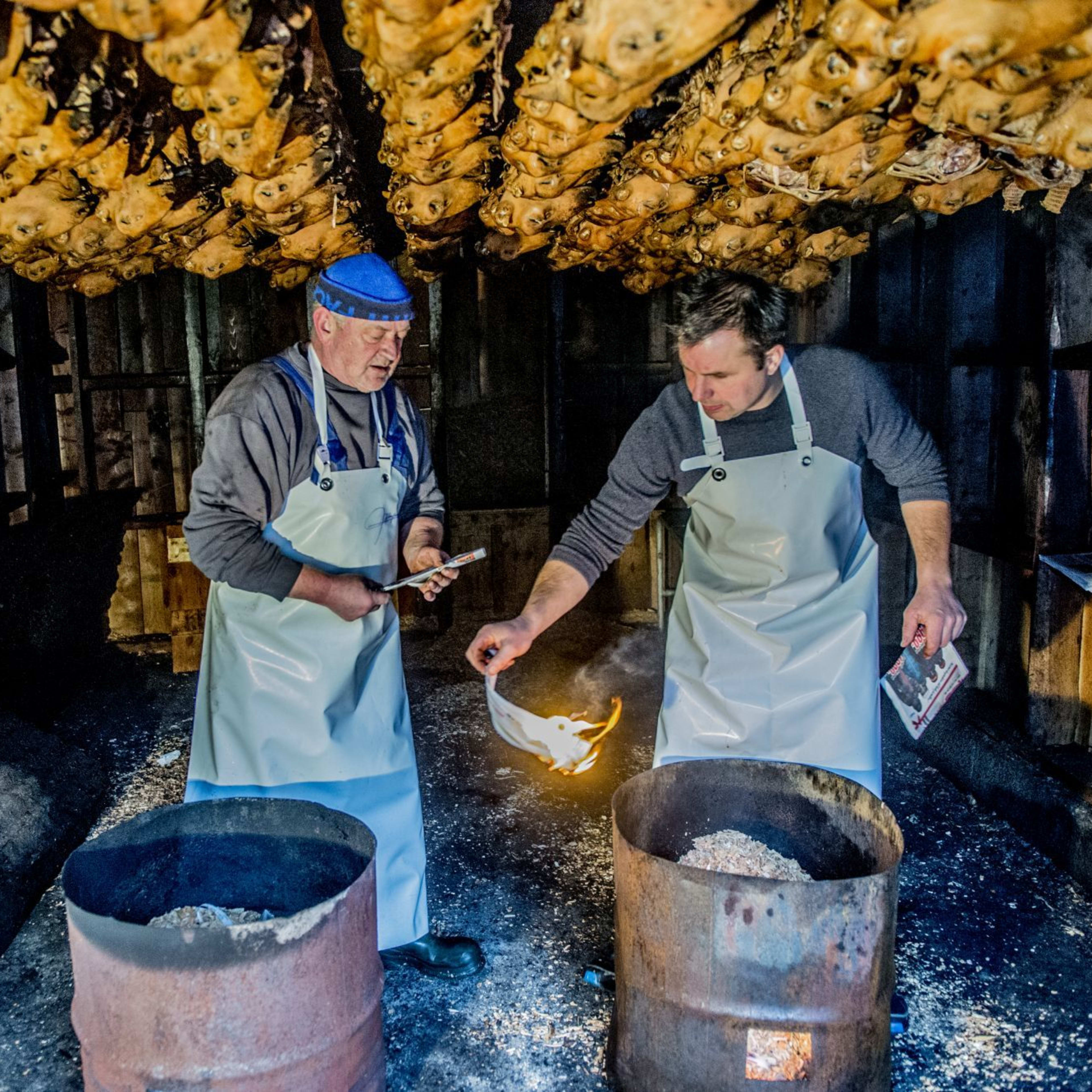 En tradisjonell norsk smalahoveprosess med to menn som kurere fisk i et rustikt røykeri, forbeholder torsk.