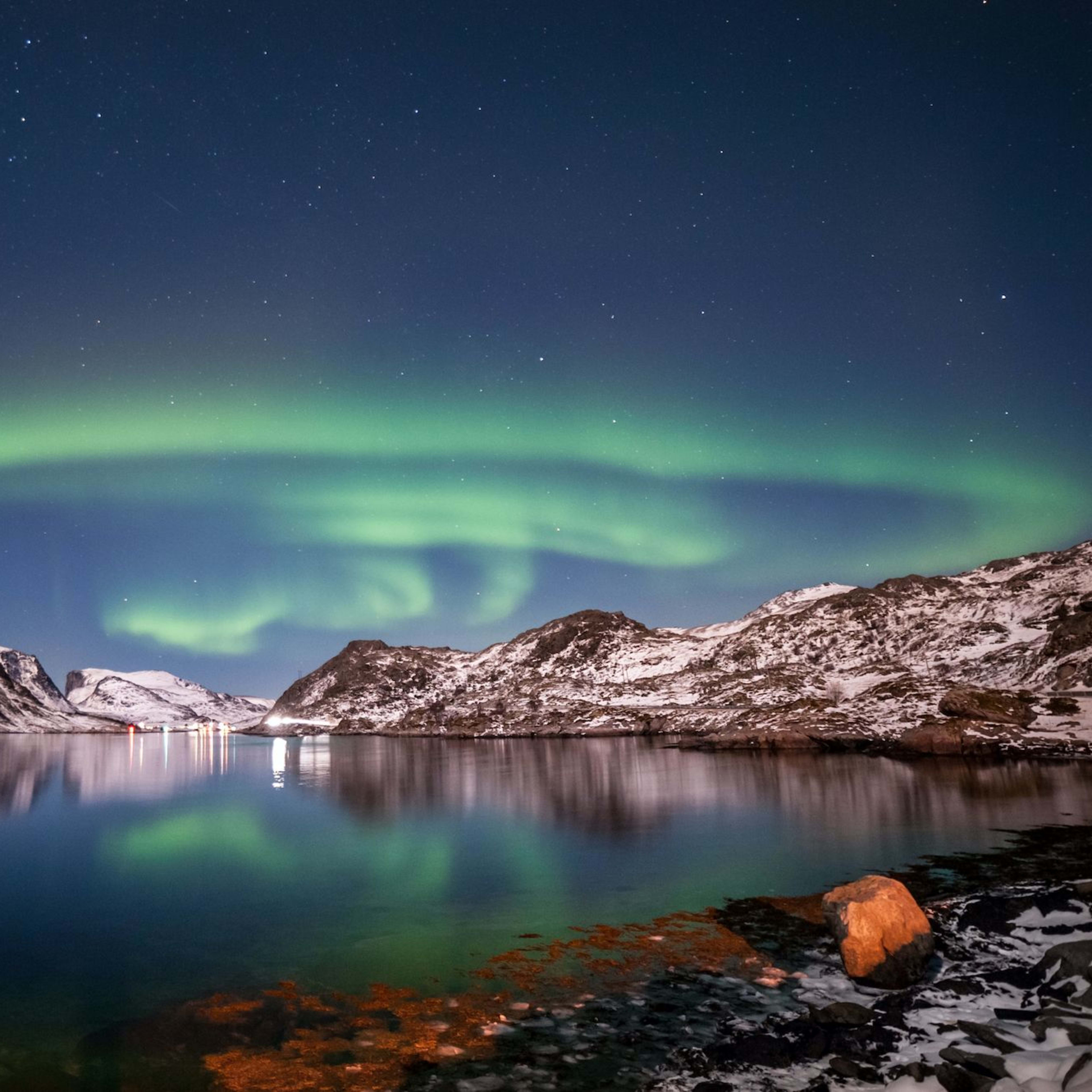 Breathtaking Northern Lights (Aurora Borealis) illuminating the sky over snow-covered mountains and still waters.
