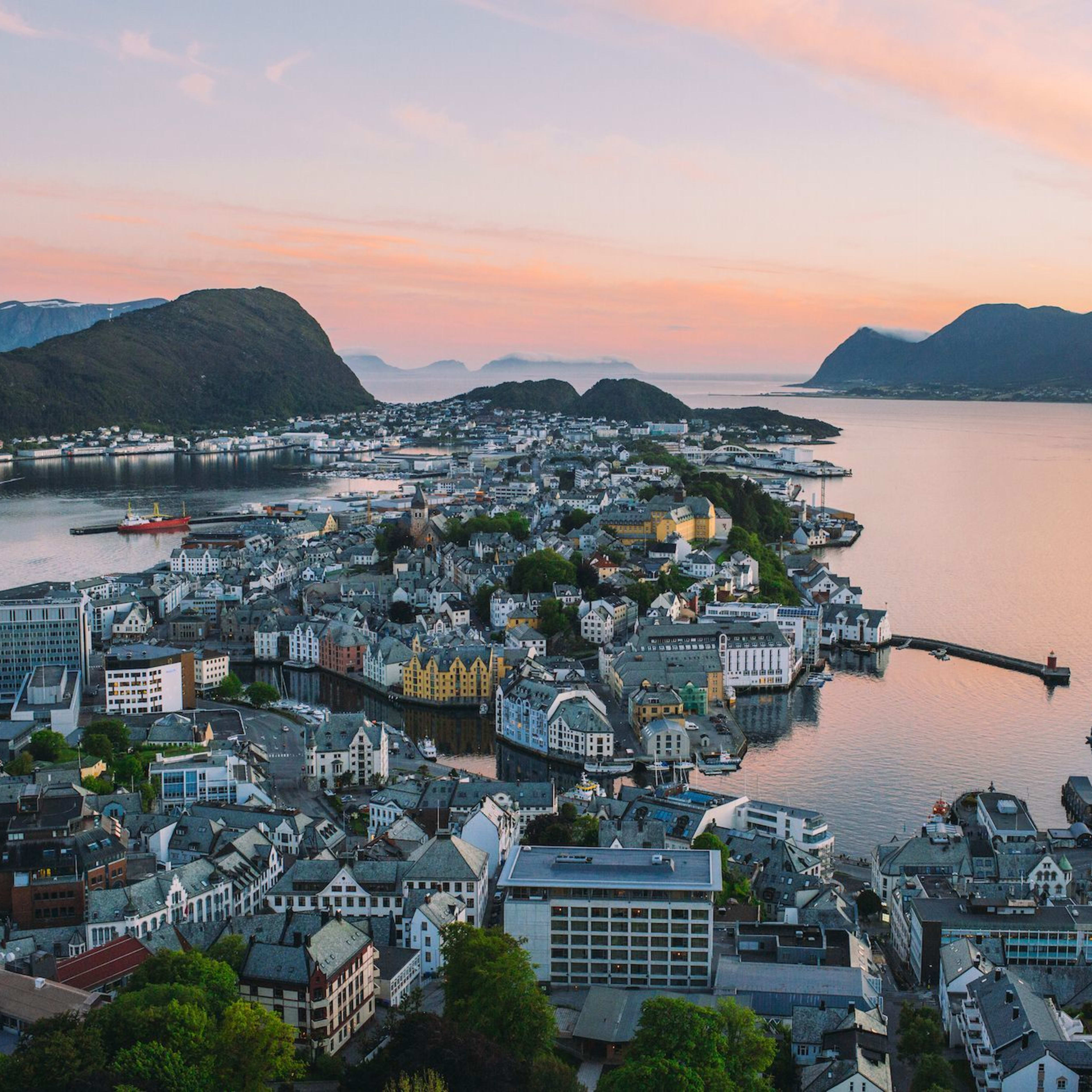 Scenic view of Ålesund, Norway, with colorful buildings, Art Nouveau architecture, and harbor under soft sunset light.