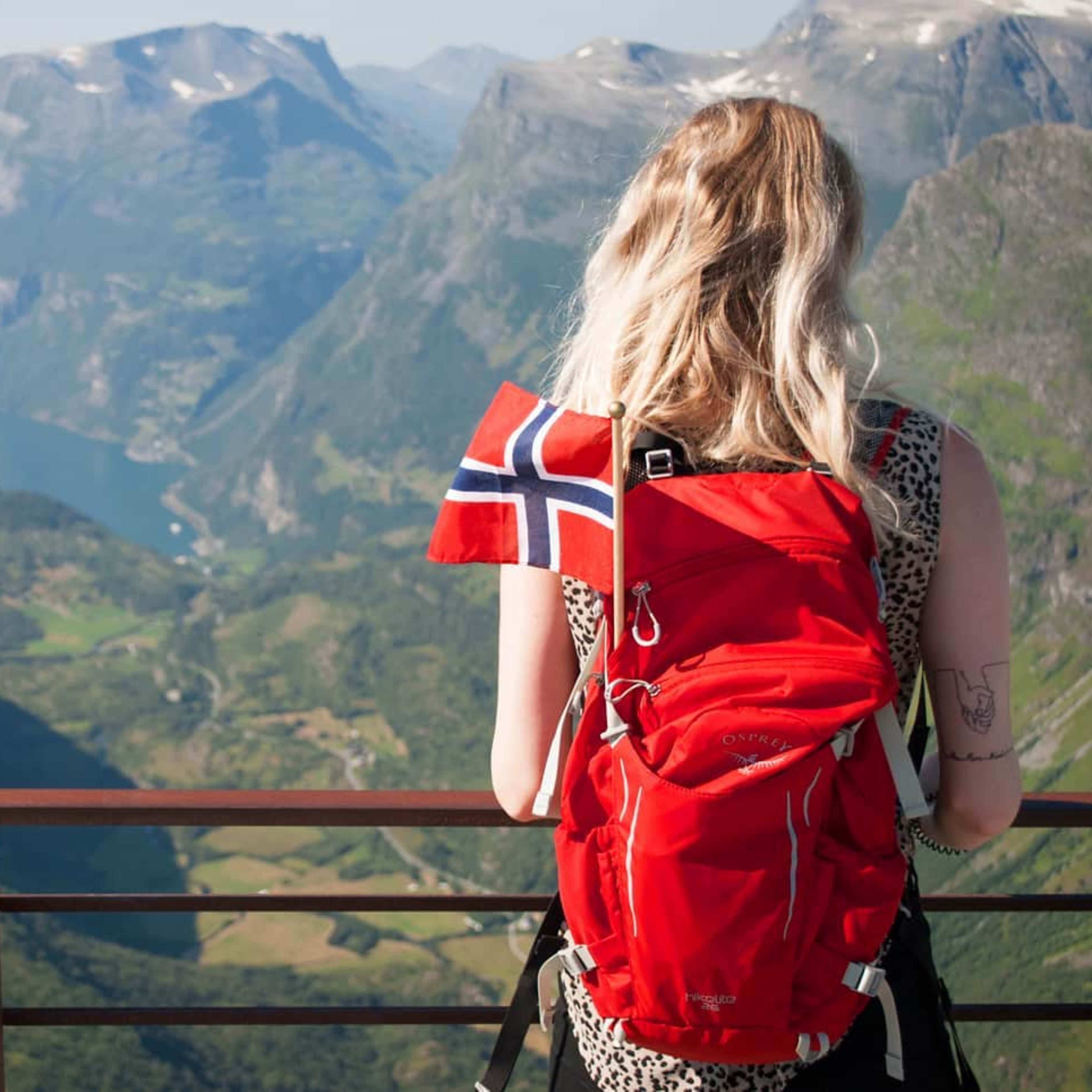 Jente som overser Geiranger og Geirangerfjorden med et norsk flagg i sekken