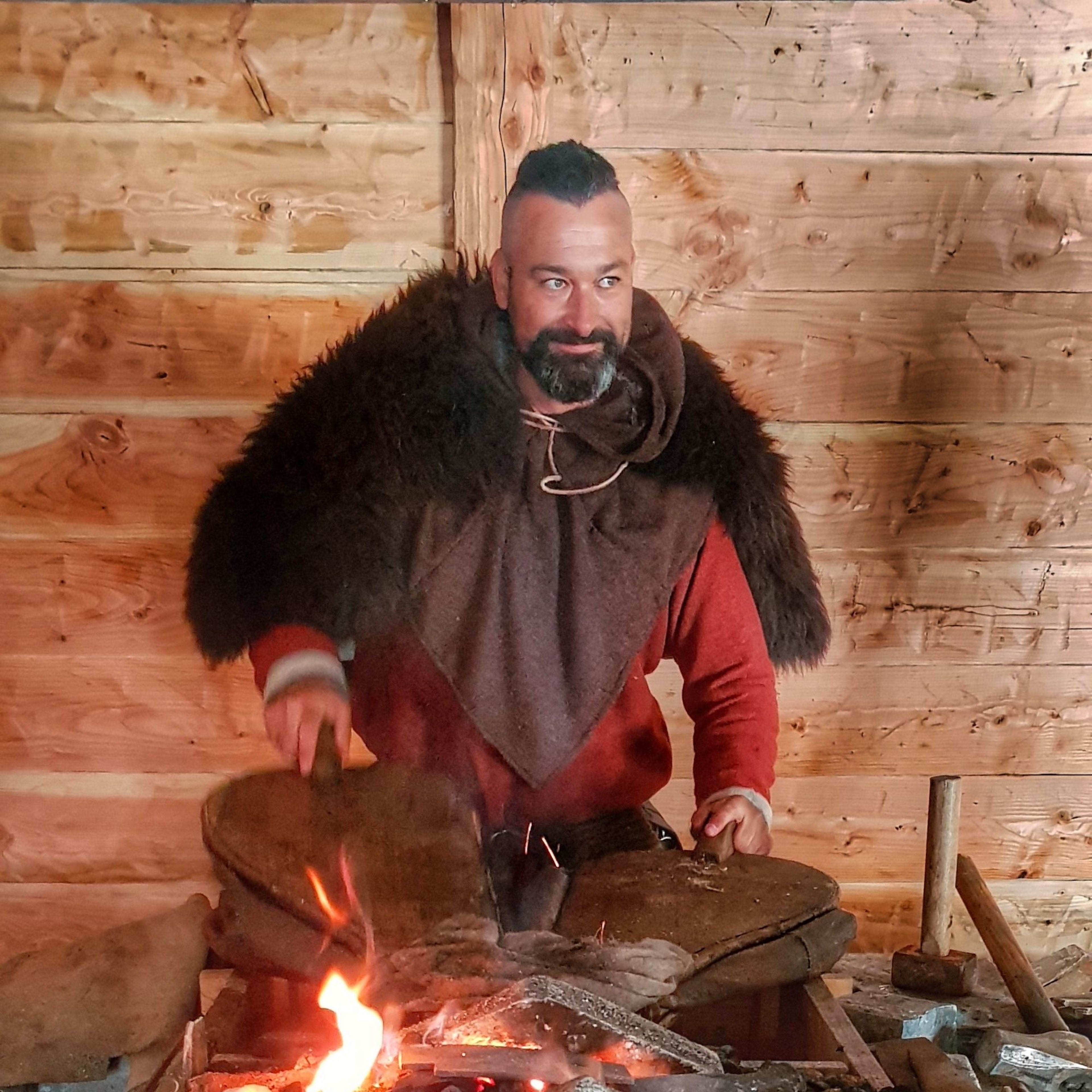 A Viking blacksmith in a fur cloak works at a forge, sparks flying as he hammers iron.