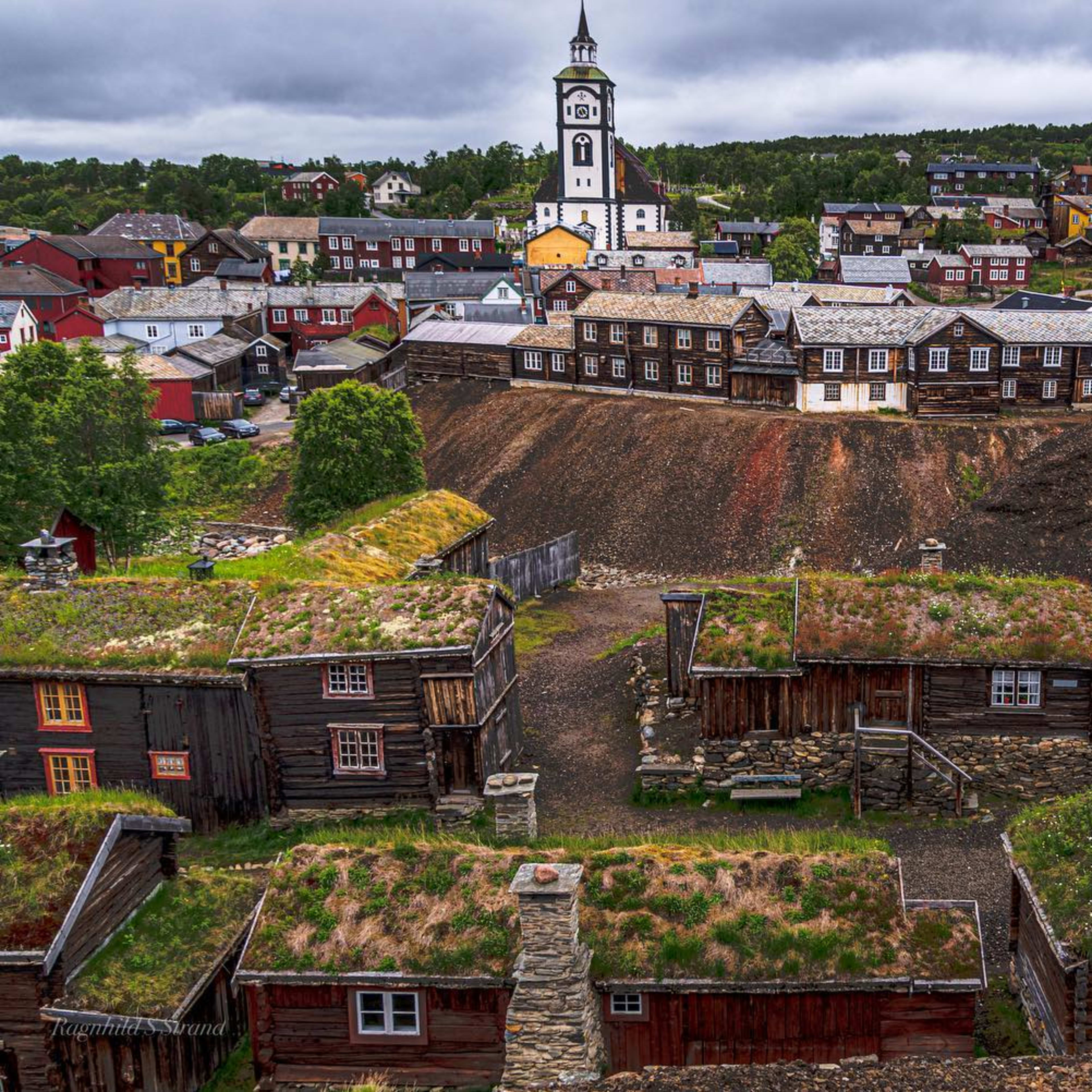 Historisk by med trehus og torvtak under skyet himmel.