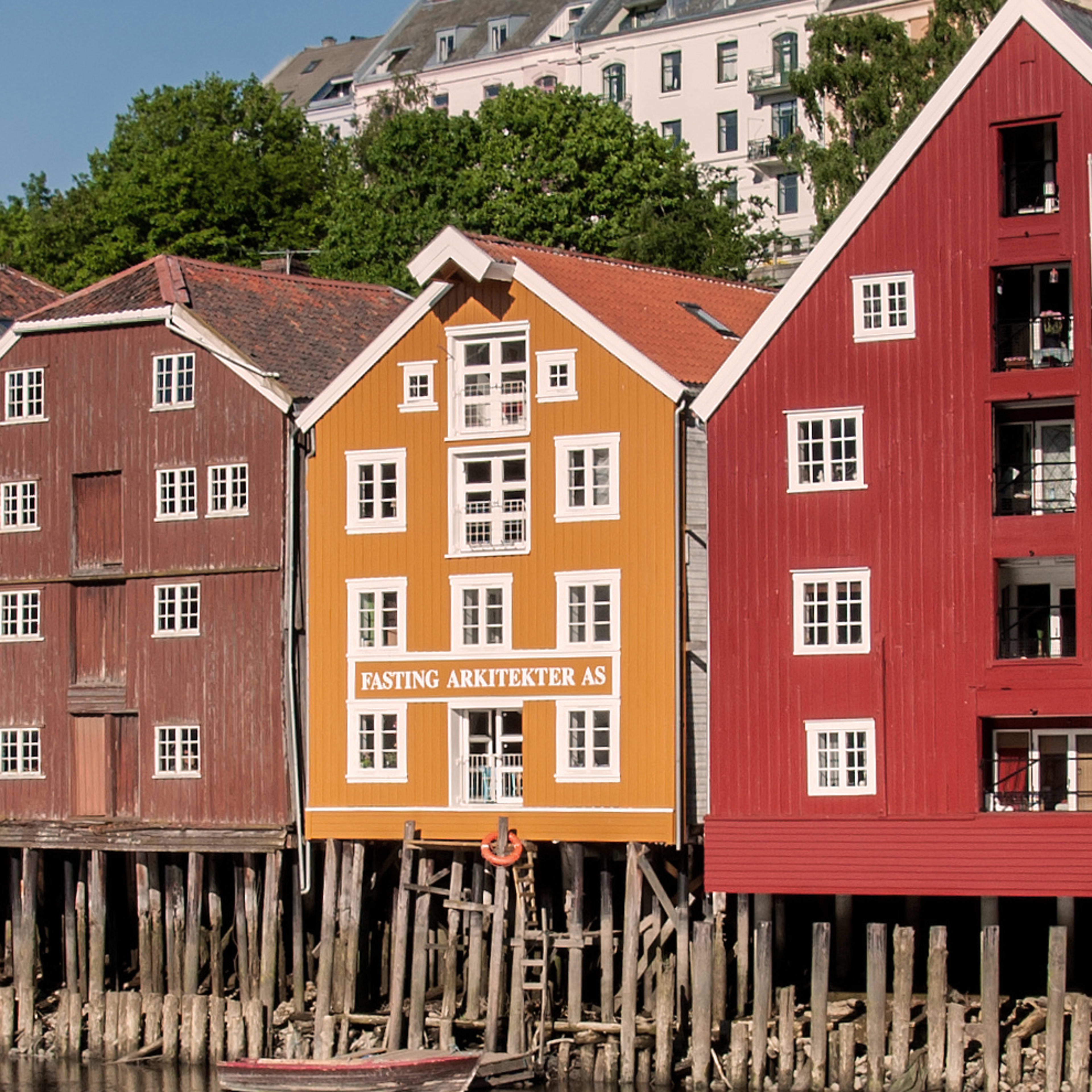 Fargerike trehus langs elven Nidelva i Trondheim på solskinnsdag med stille vannspeil