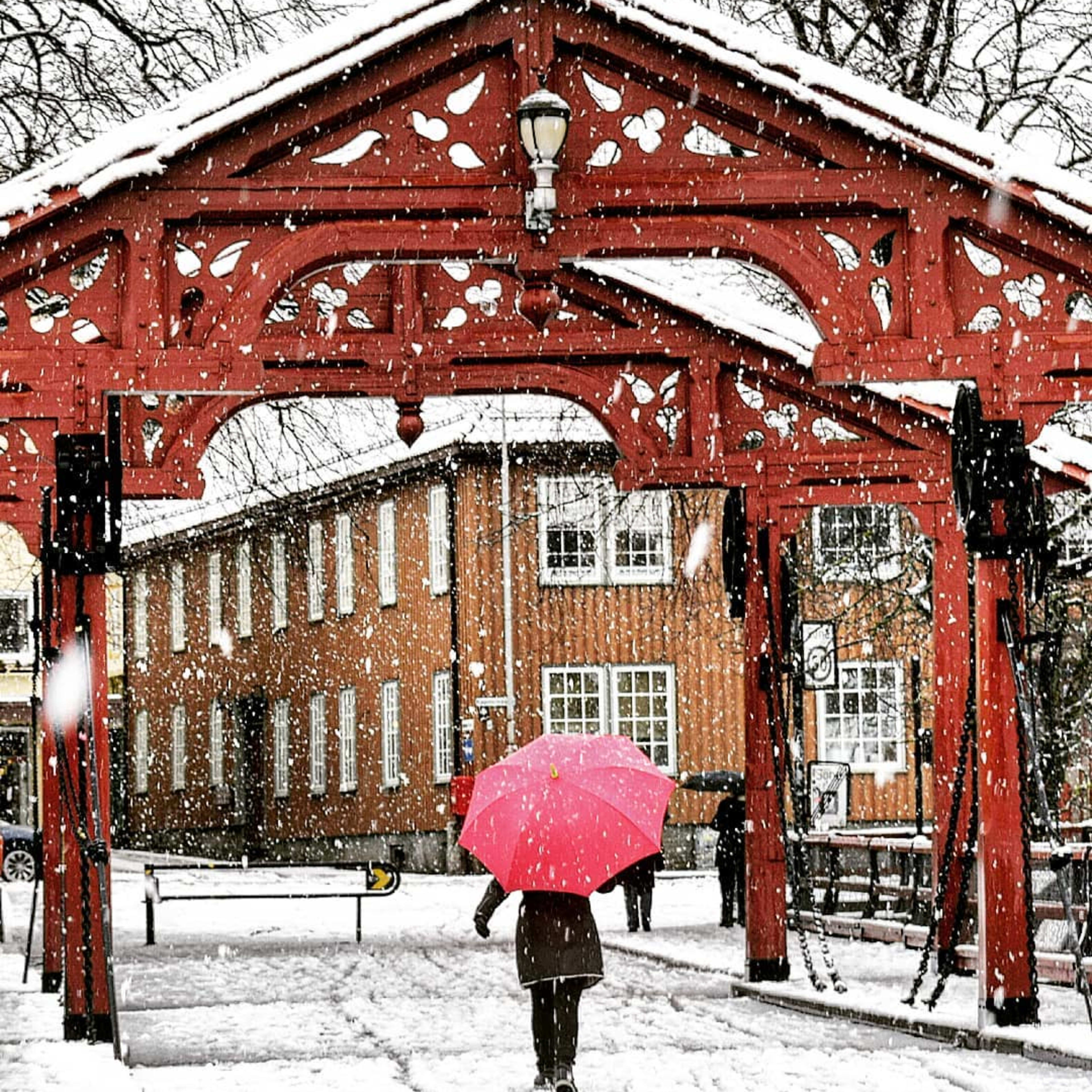 Person med rosa paraply går gjennom rød port i kraftig snøvær.