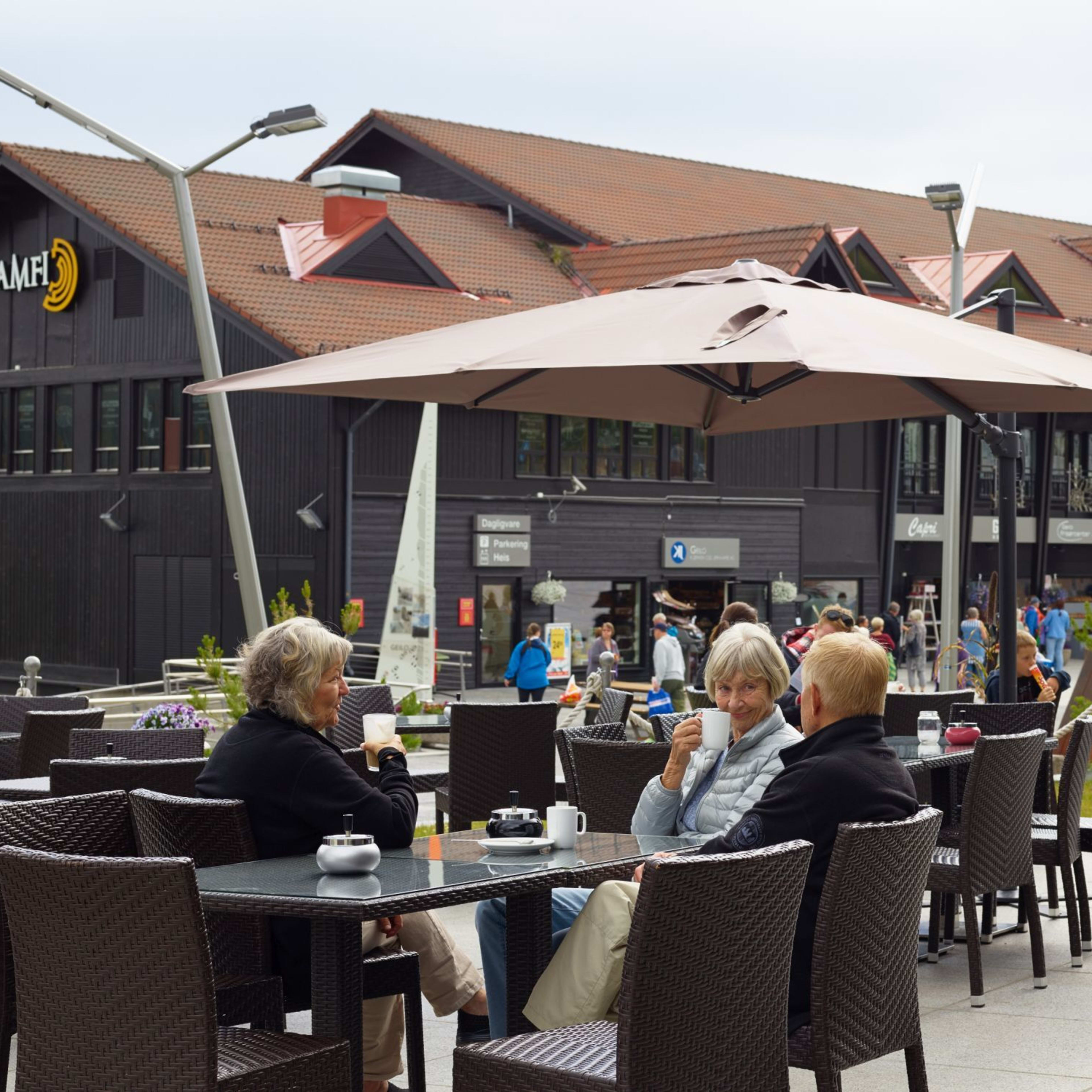 People enjoy drinks at outdoor café near shopping center with wood buildings.