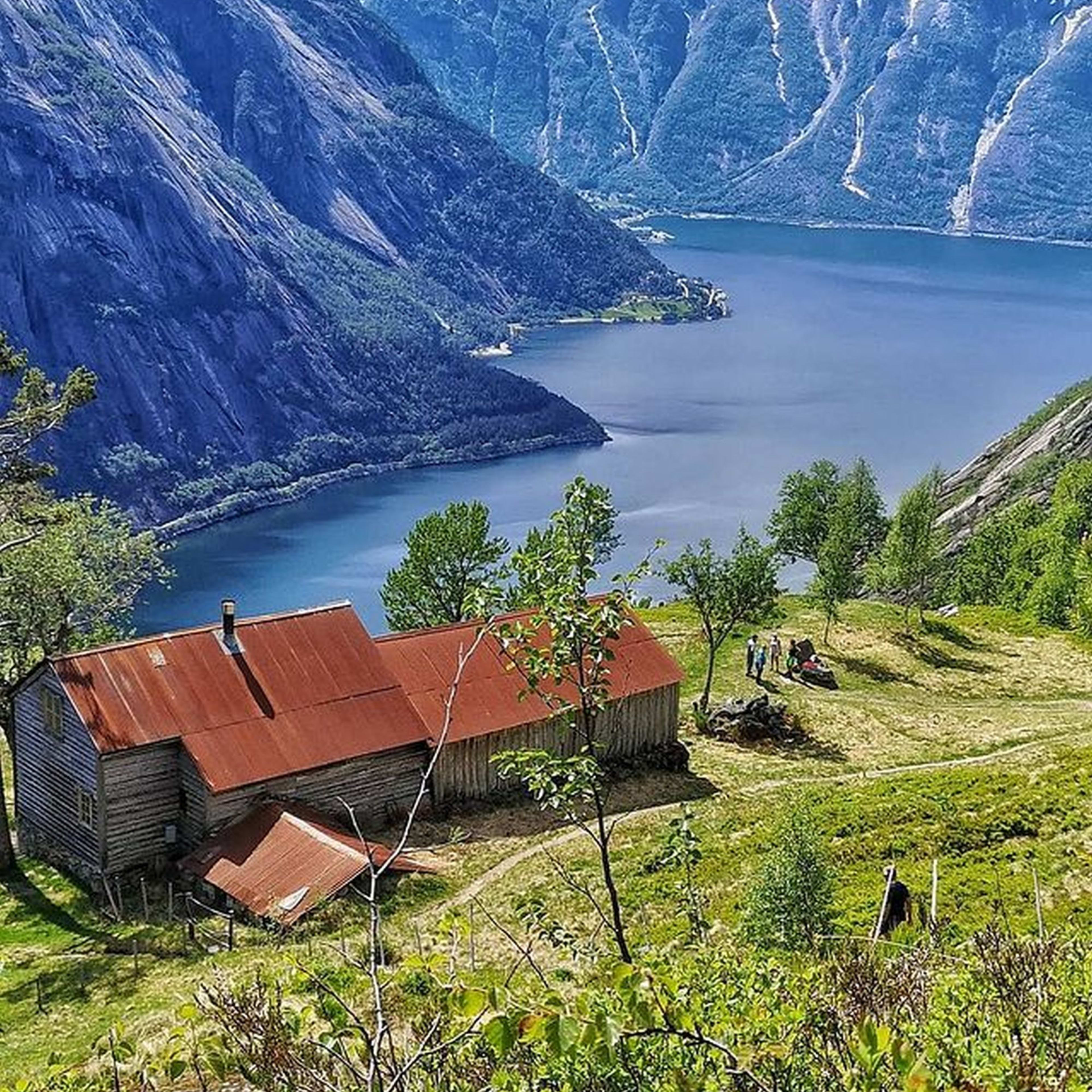 Ein Bauernhaus mit rotem Dach auf einem grünen Hügel, mit Blick auf einen Fjord und schneebedeckte Berge.