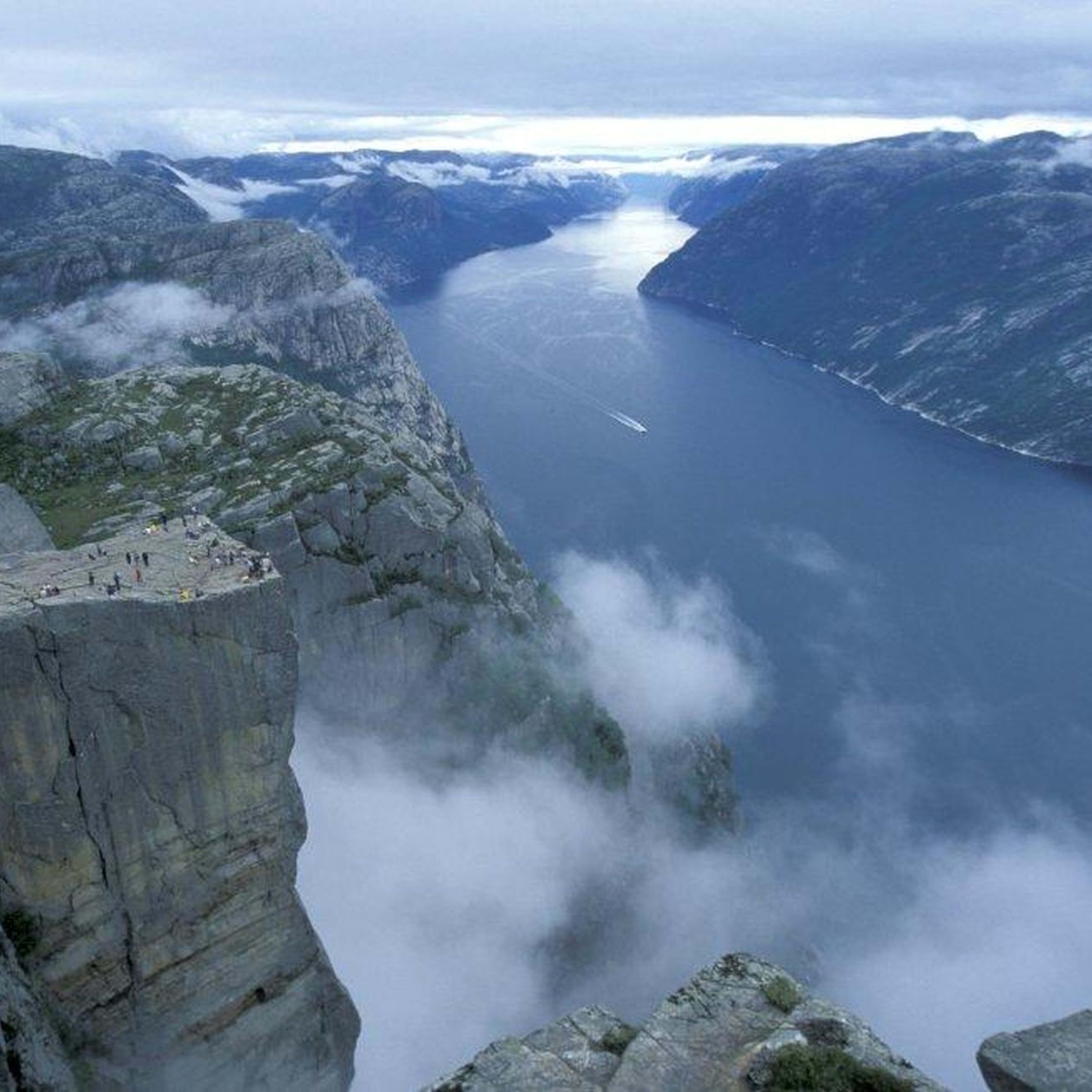 Luftaufnahme von Preikestolen (Predigtstuhl), mit Menschen auf der Klippe, nebligen Bergen und Fjord im Hintergrund.