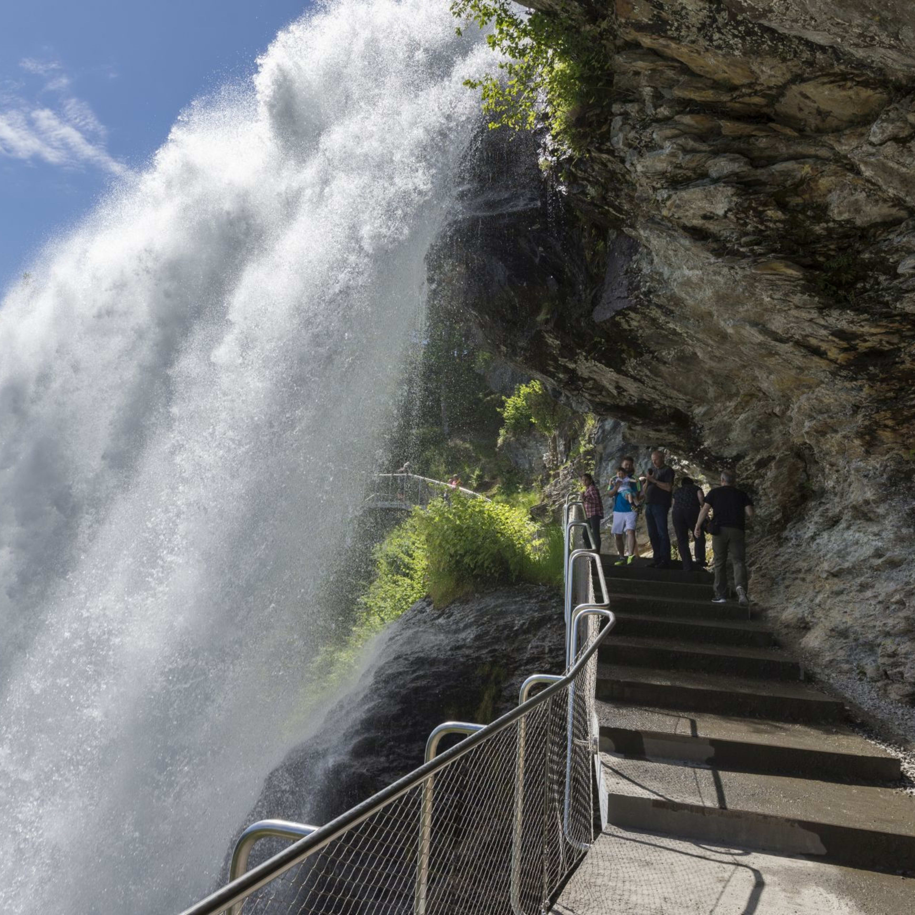 Touristen gehen Weg hinter Wasserfall in grünes Tal.