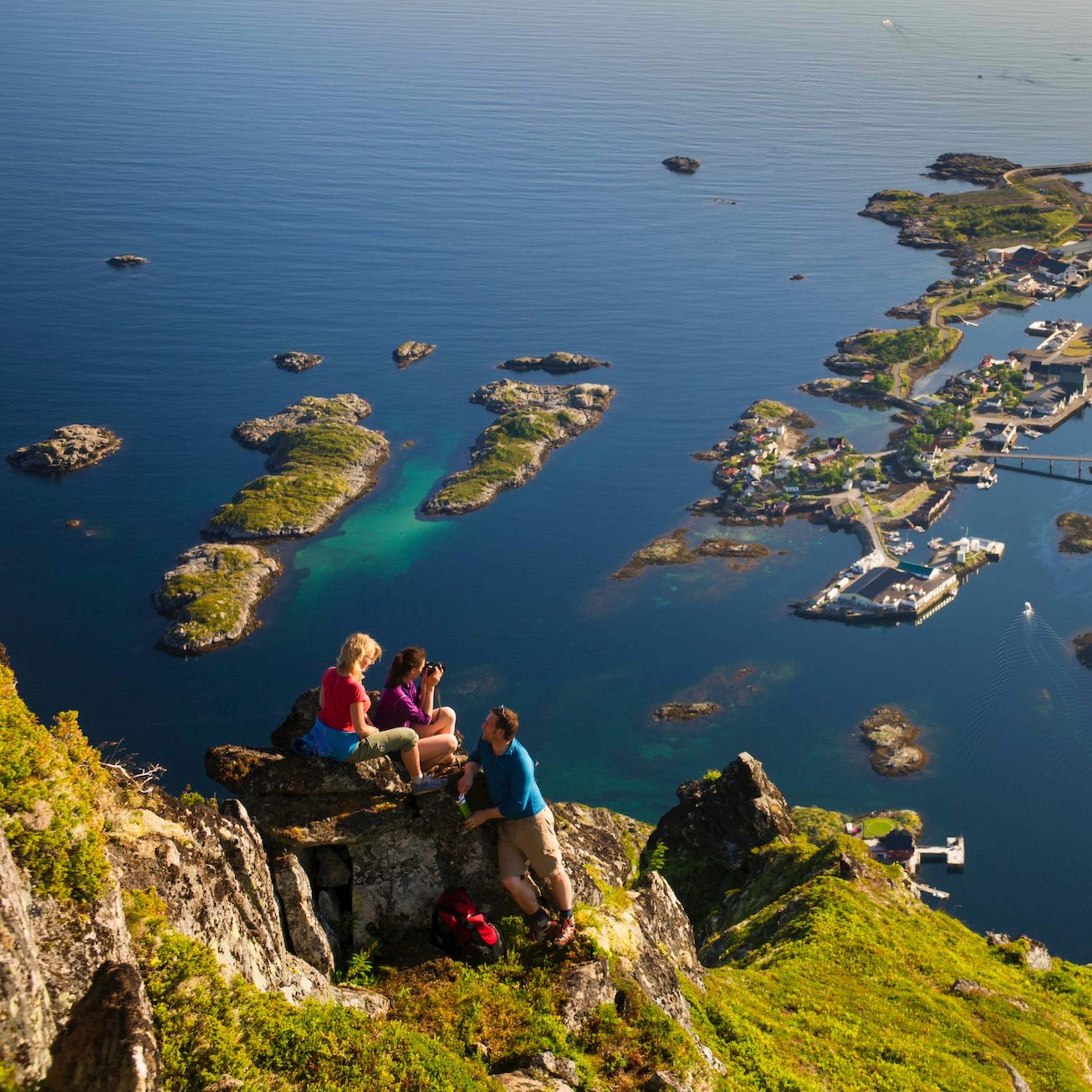 Turgåere hviler på klippe med utsikt over øyer, fjord og by.