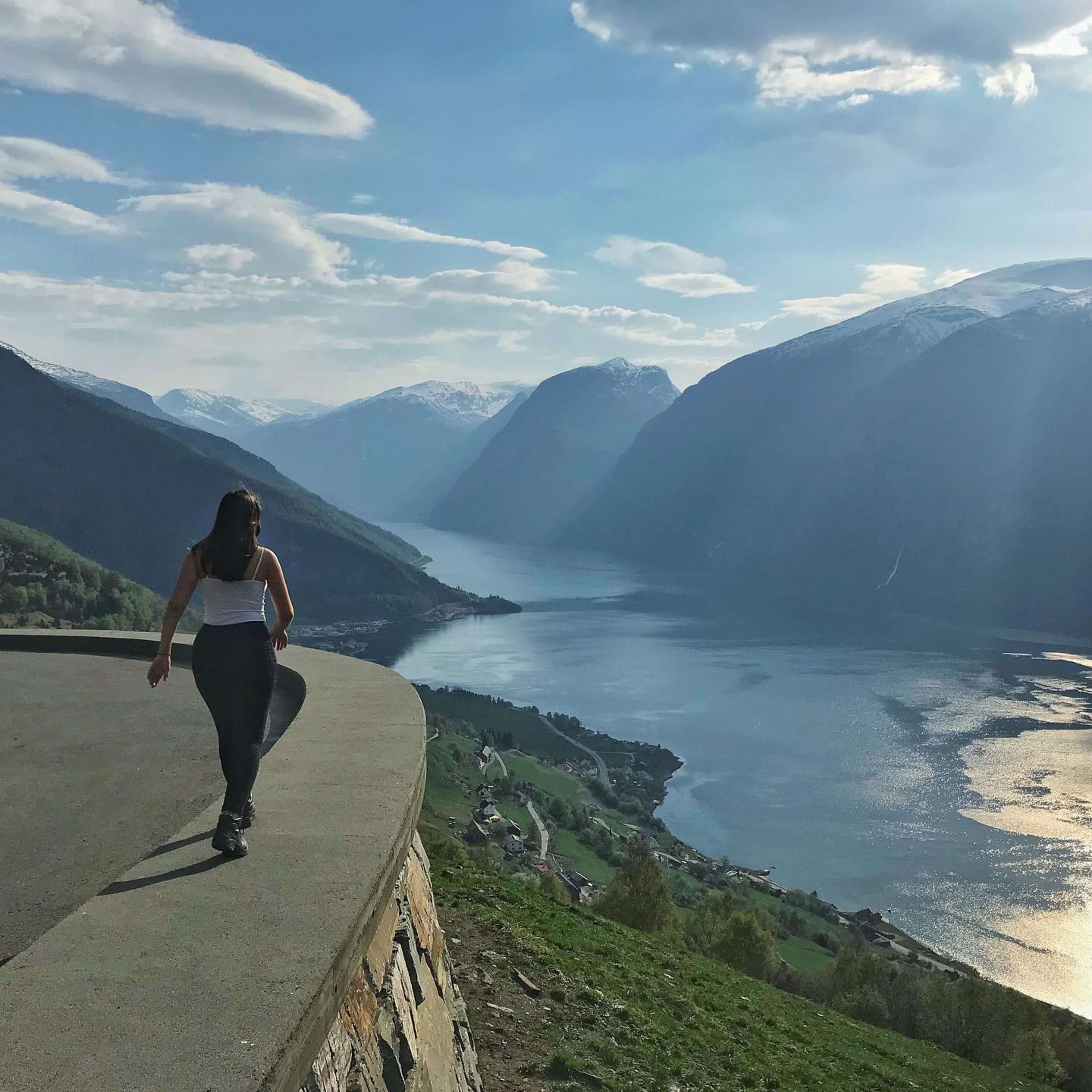 Frau geht auf Plattform mit Blick auf Fjord und schneebedeckte Berge.
