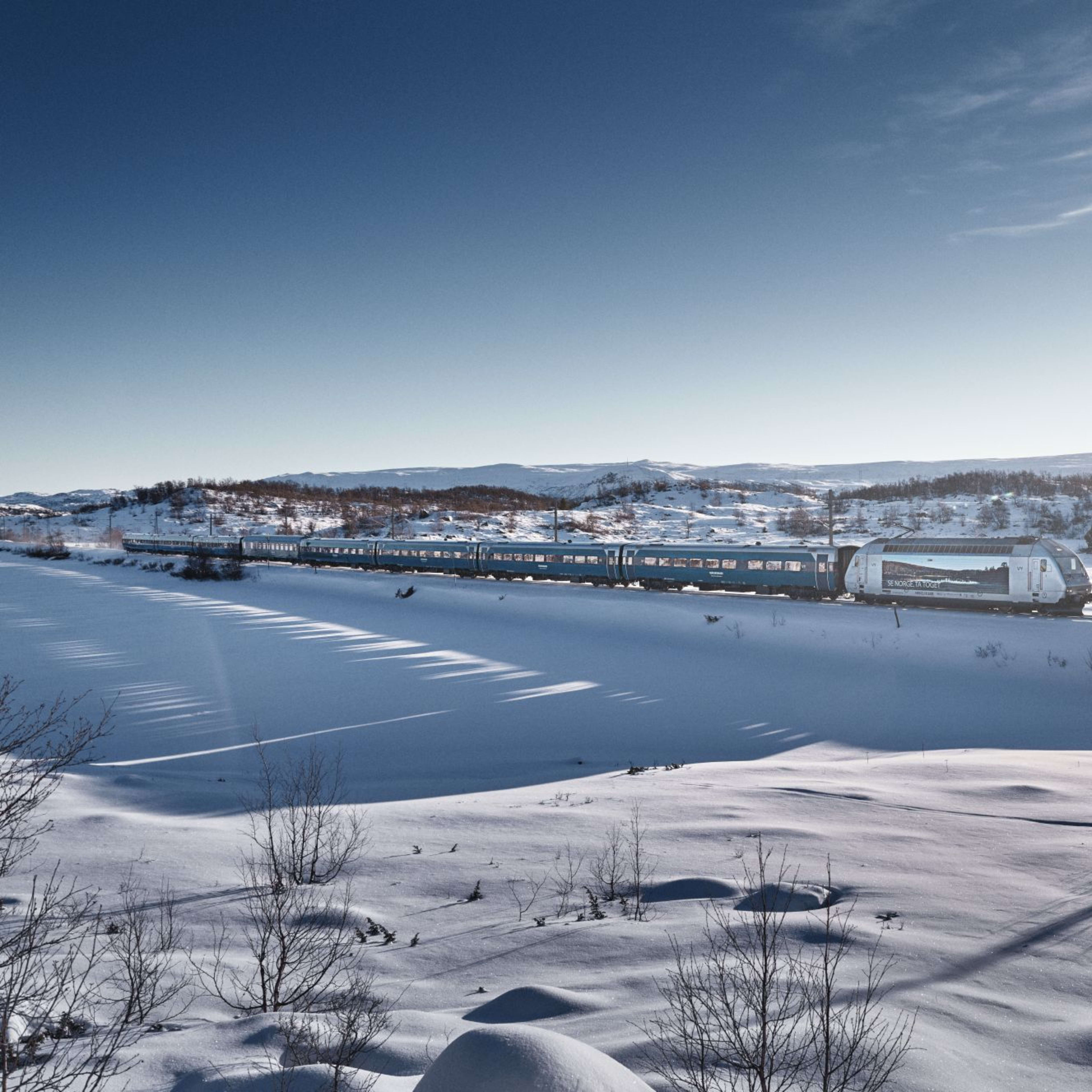 Zug im Schnee mit langen Schatten und blauem Himmel.