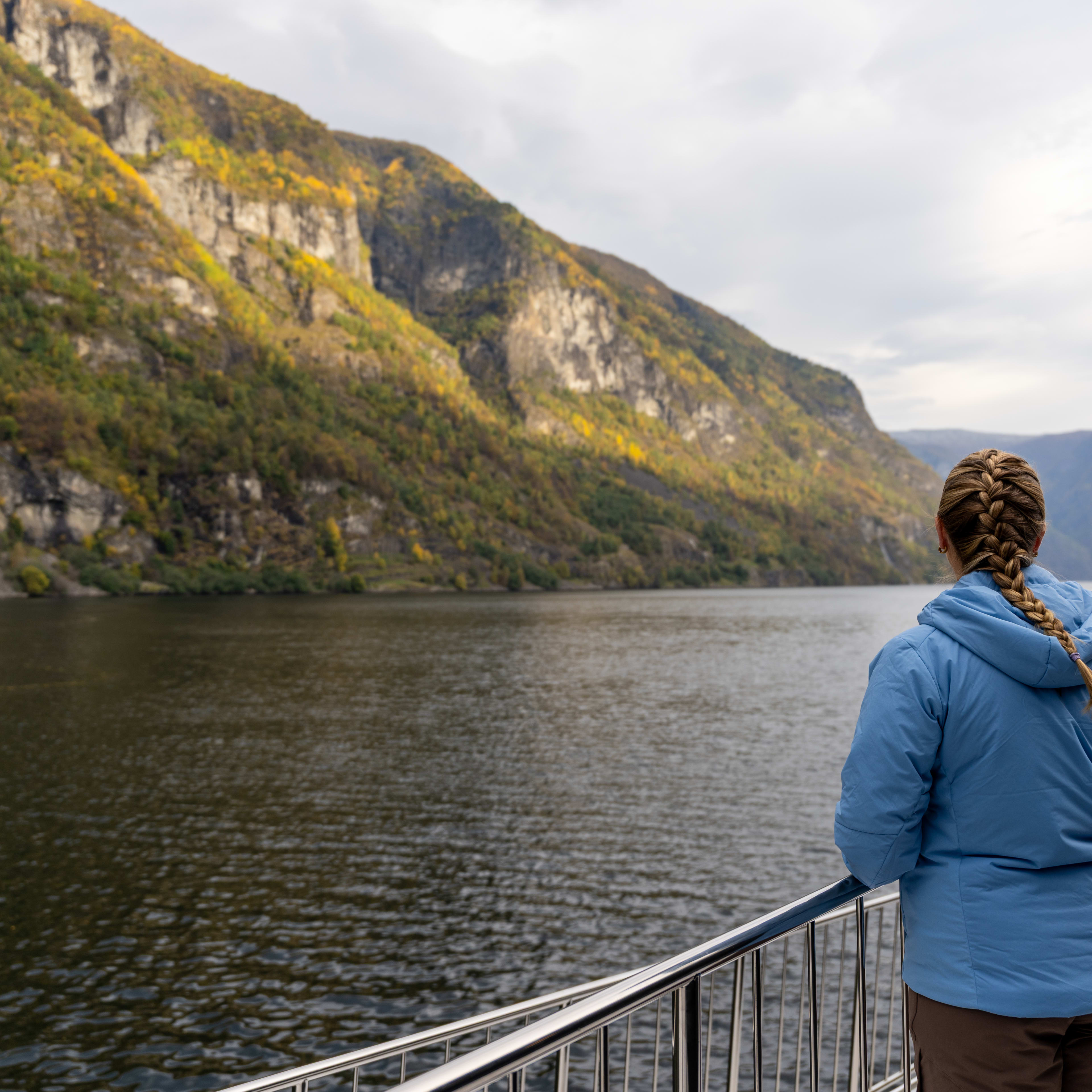 Frau genießt den Blick auf den Nærøyfjord in herbstlichen Farben während einer Fjordkreuzfahrt ab Flåm.