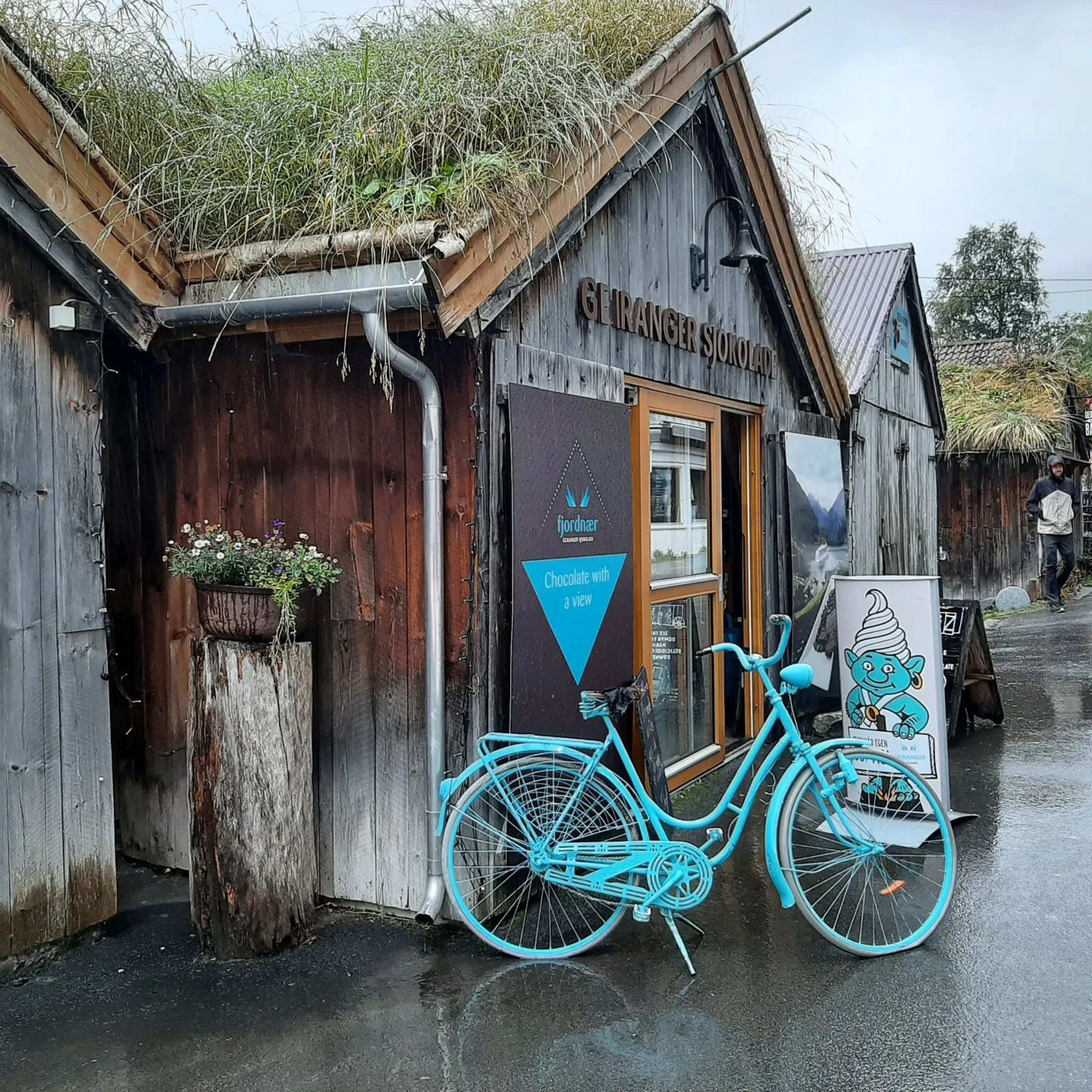 Blå sykkel ved tradisjonelt trehus i Geiranger, UNESCO-beskyttet fjordområde på Vestlandet