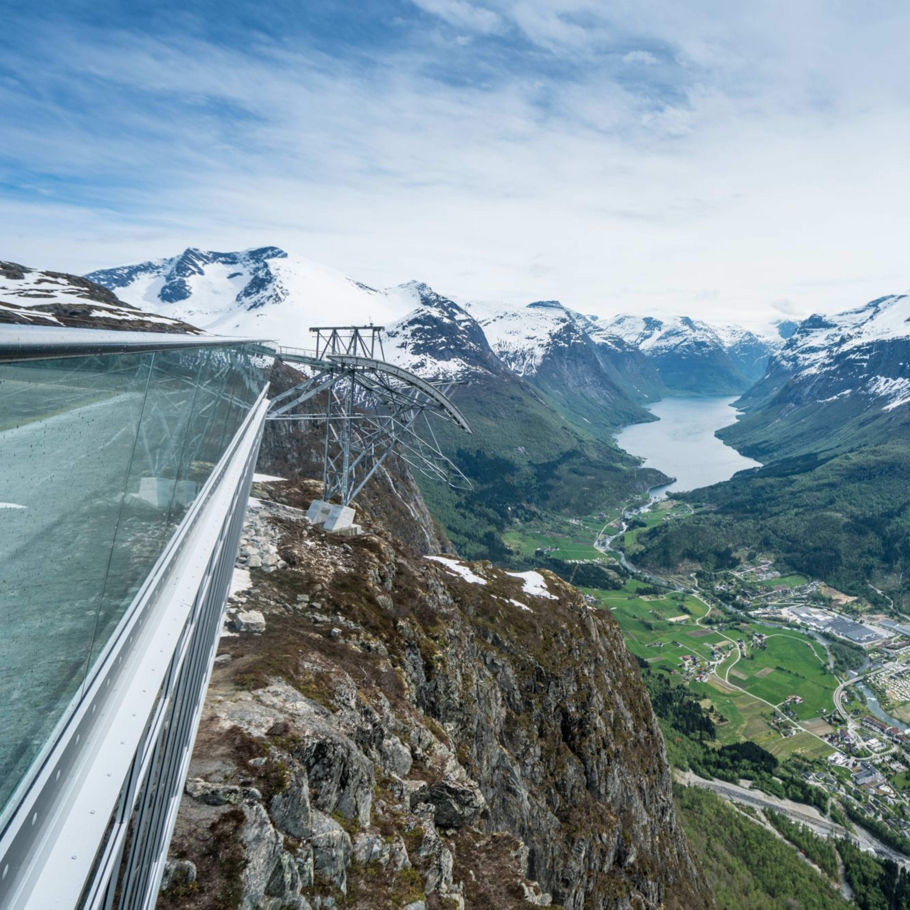 Utsikt fra glassplattform over fjord og snødekte fjell.