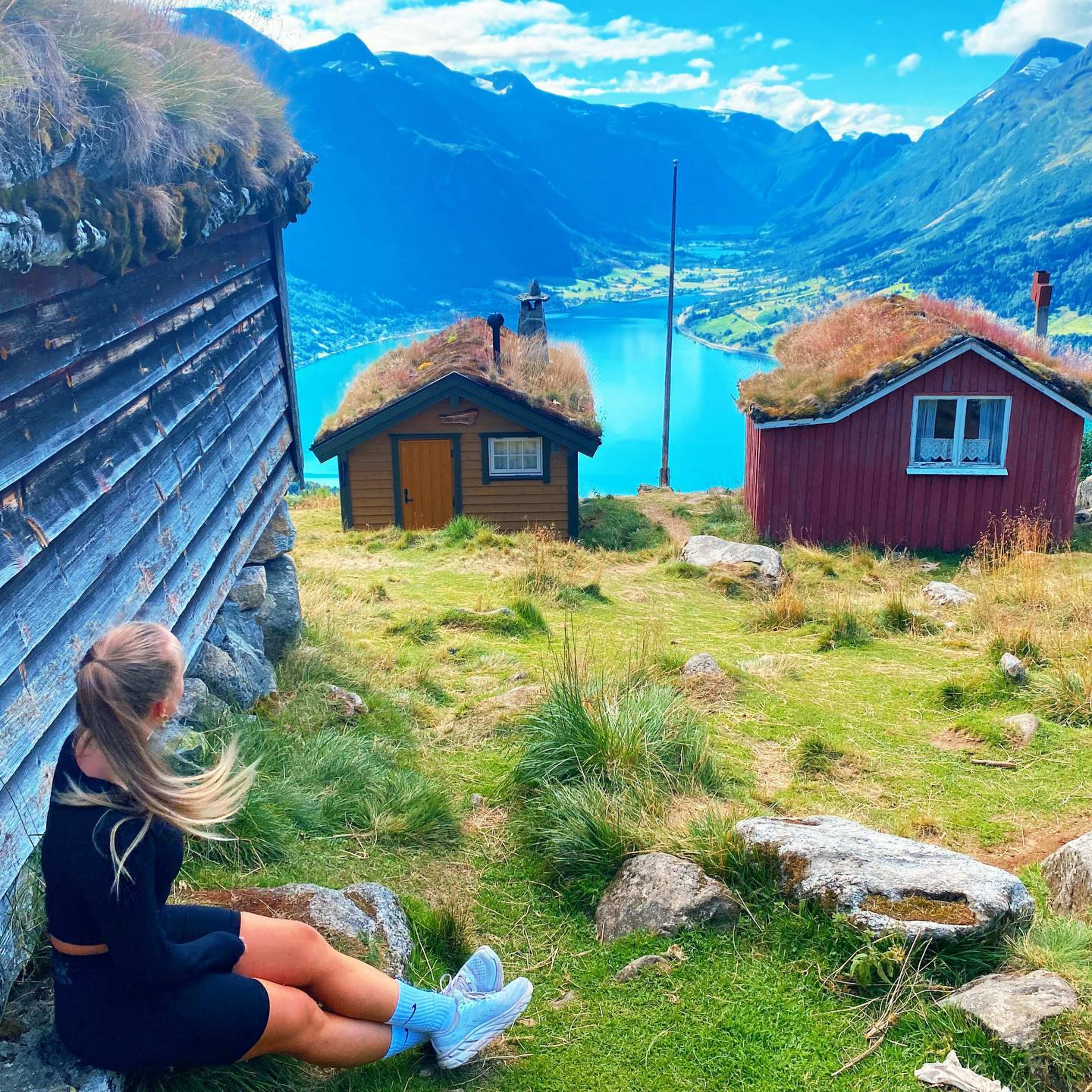 Kvinne ser mot blå fjord fra torvhyttene.