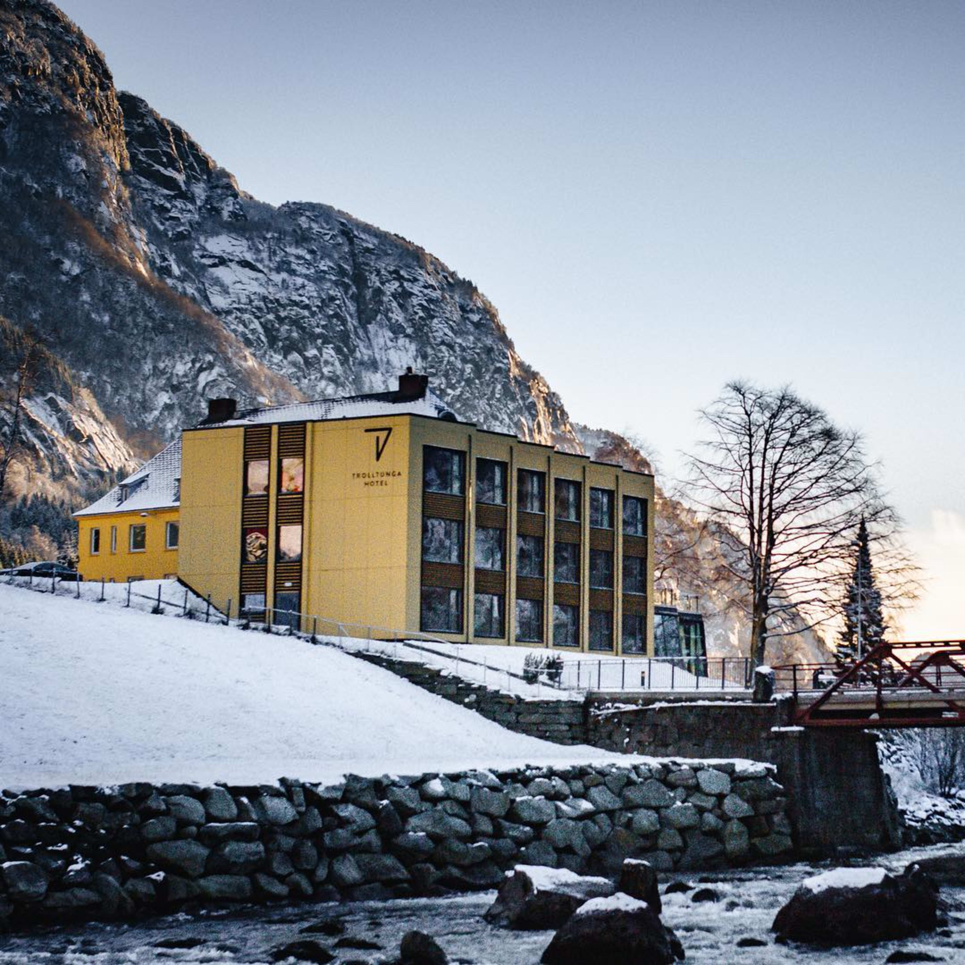 Gelbes Hotel bei Fluss und roter Brücke im verschneiten Gelände.