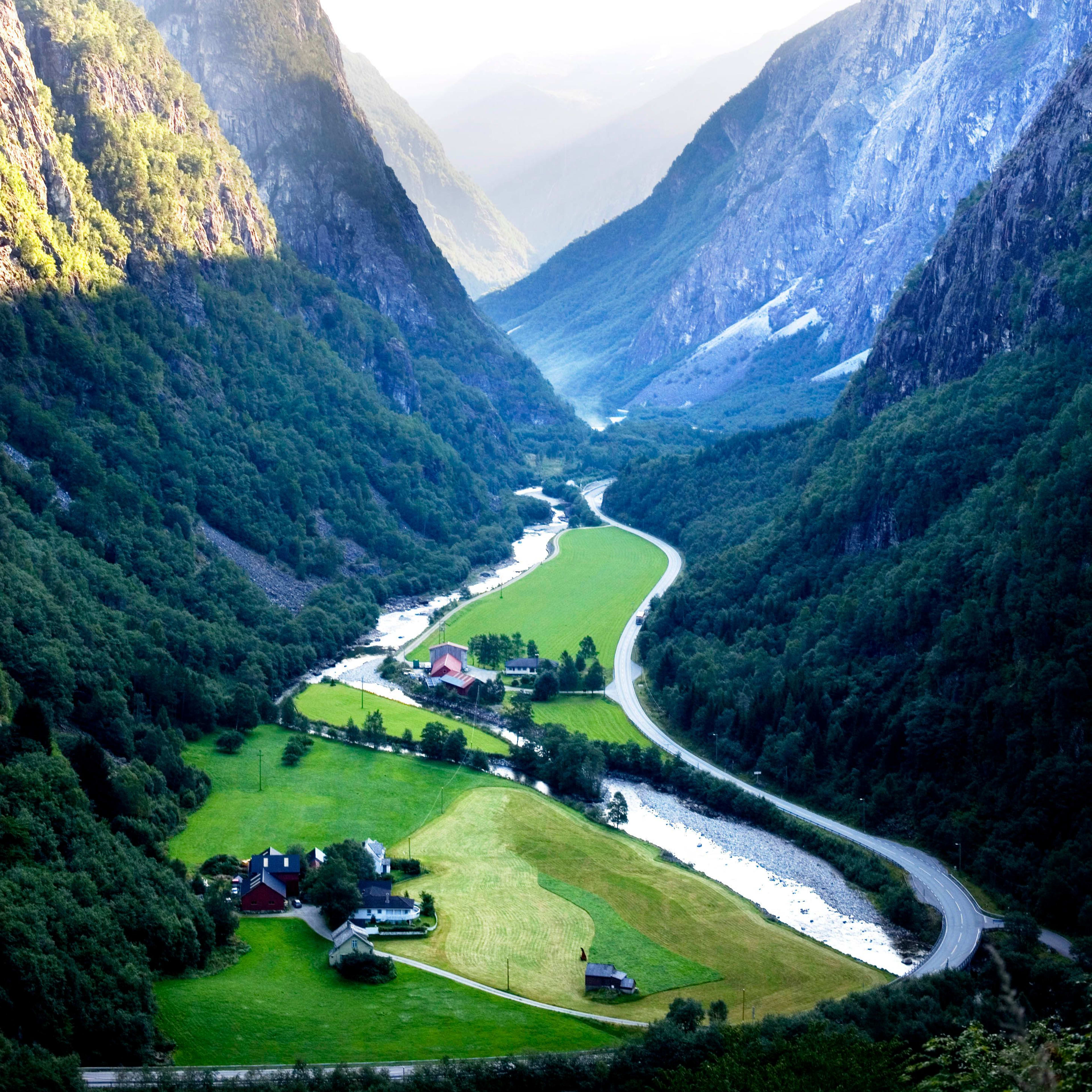 Green valley with river, farms, cliffs, and misty mountains.