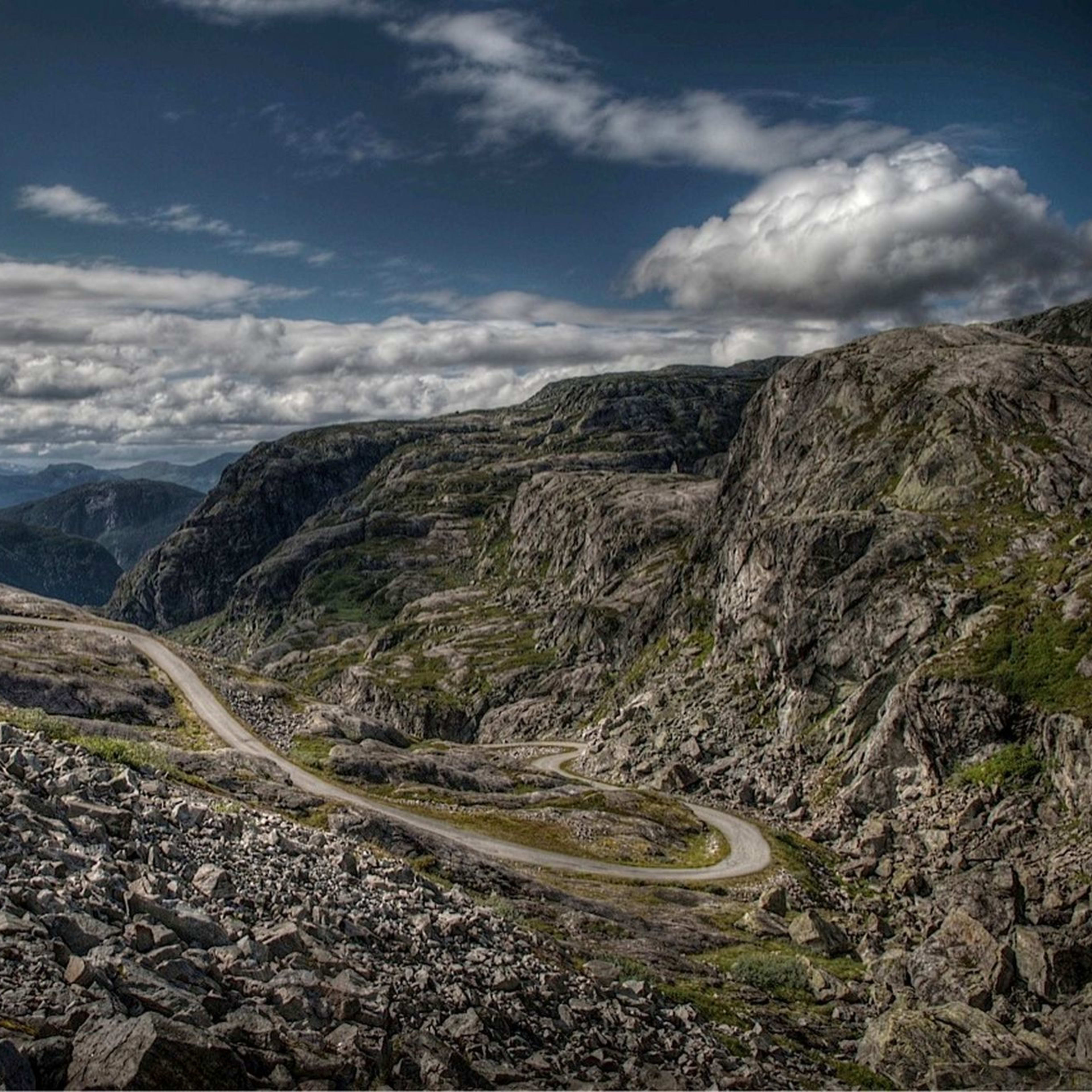 Svingete fjellvei krysser steinlandskap under dramatisk himmel.