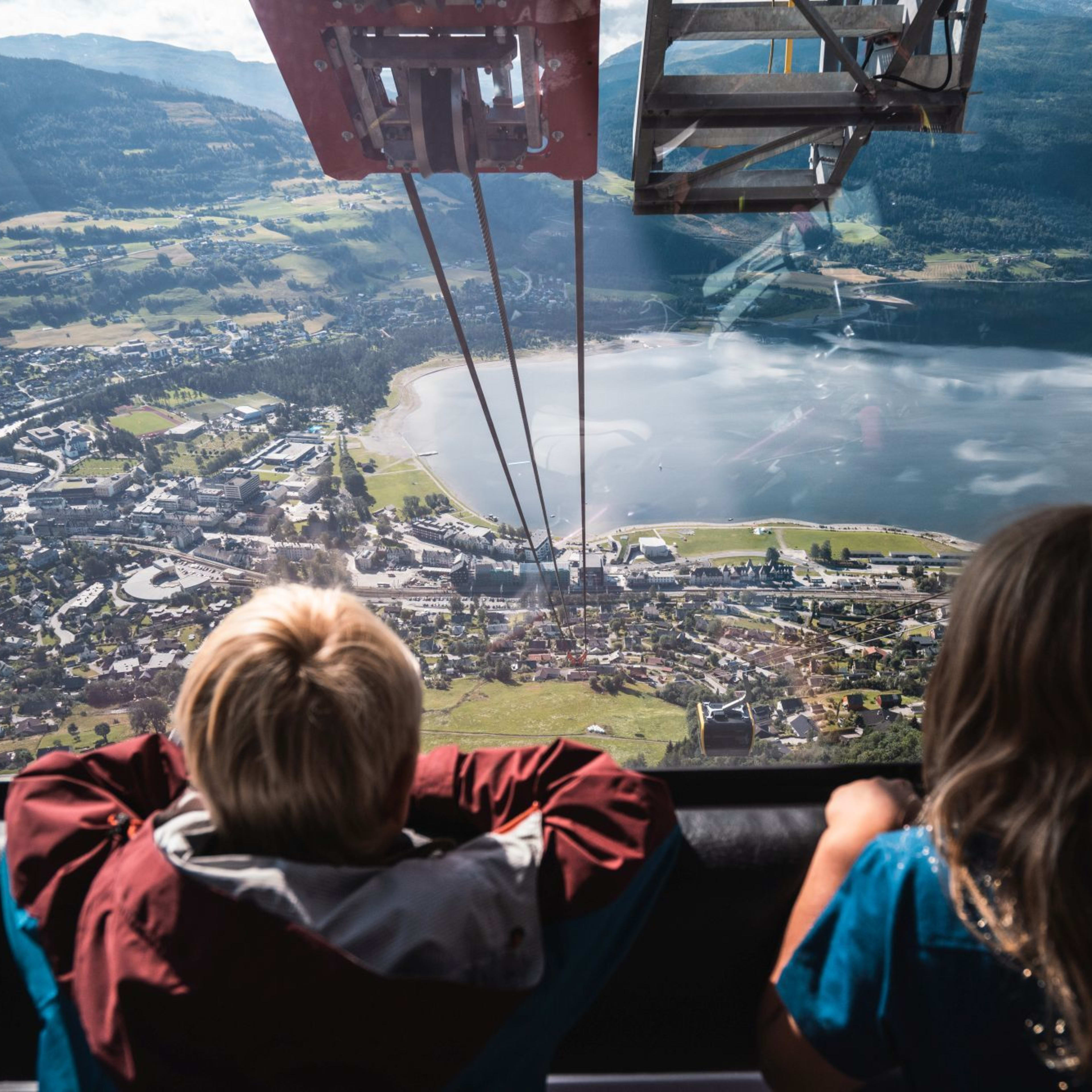 Children look out from a cable car at a town between lake and mountains.