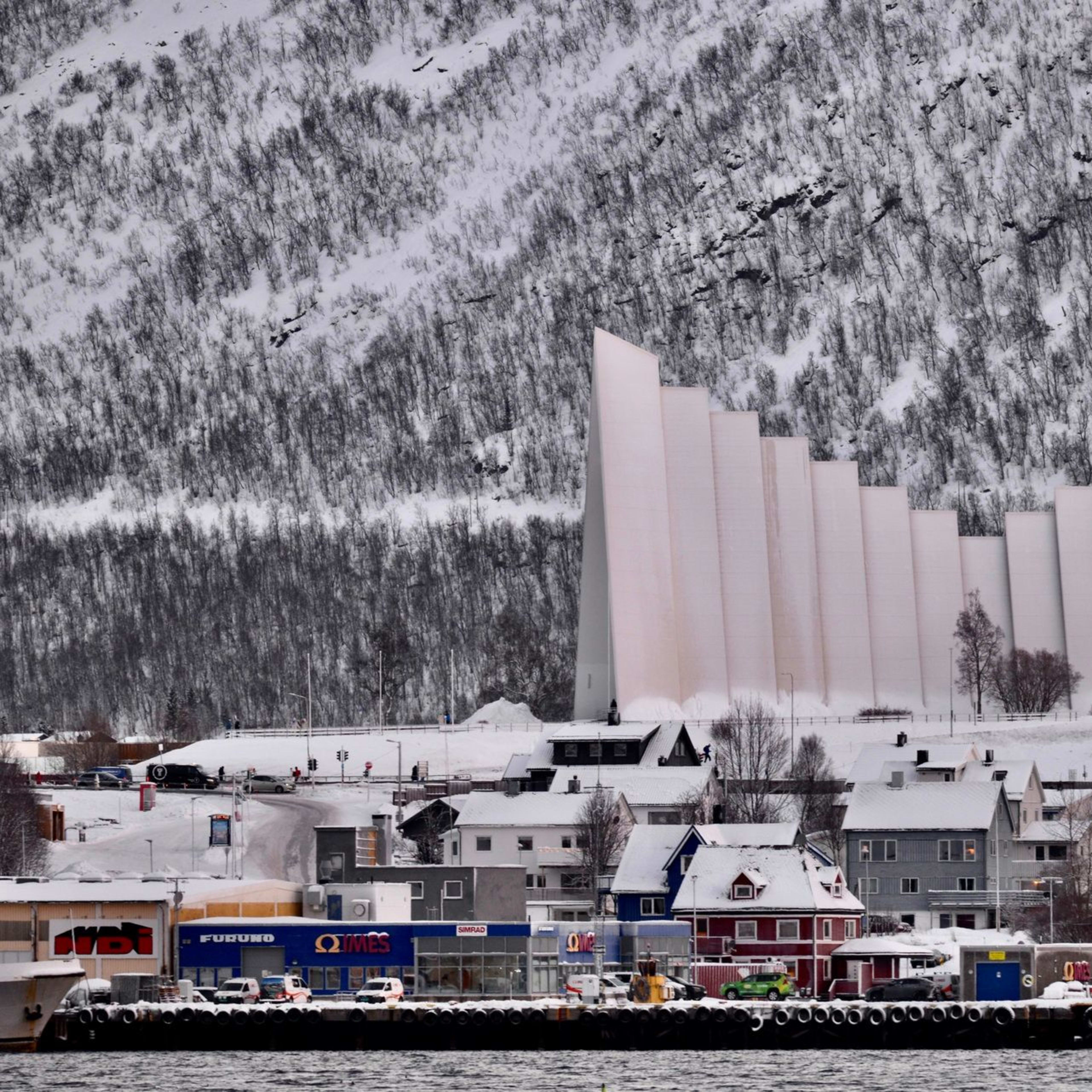 The Arctic Cathedral in Tromsø, with a snowy mountain backdrop and a colorful town below.