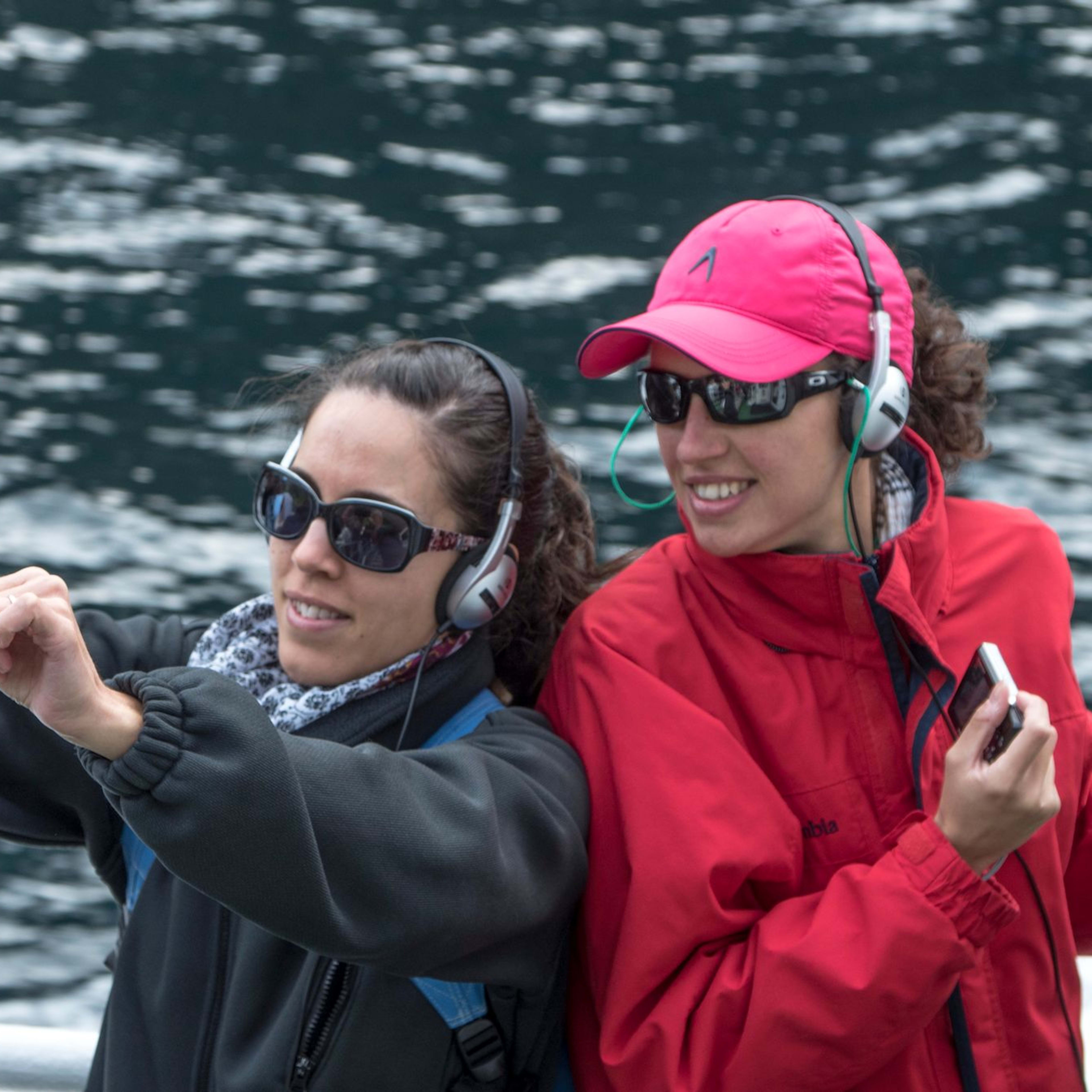Frauen mit Kopfhörern machen Selfie am Wasser auf Boot.