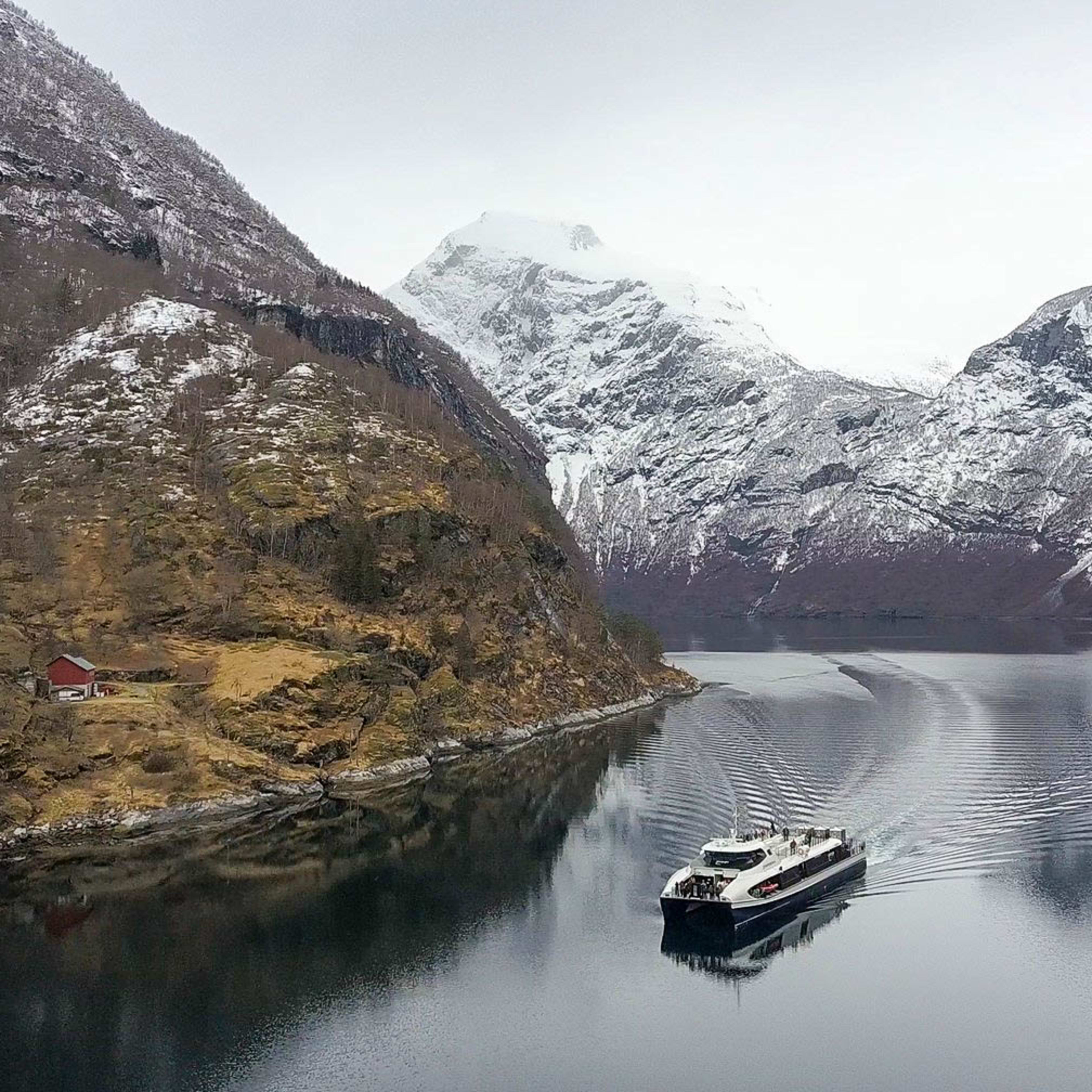 Hybrid electric boat cruising Geirangerfjord, UNESCO World Heritage fjord surrounded by snow-capped mountains.
