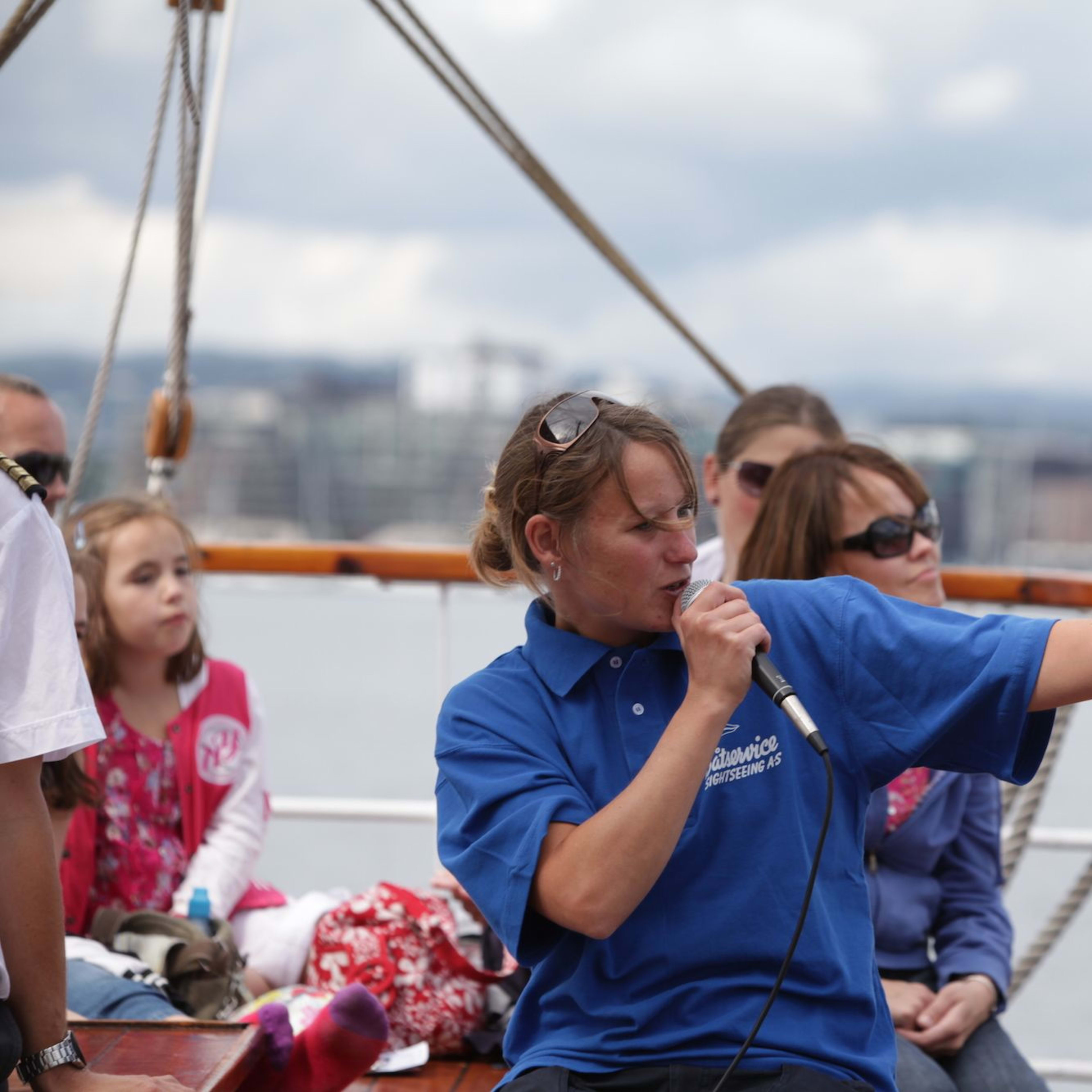 Tour guide in blue shirt speaking into mic on sightseeing boat.