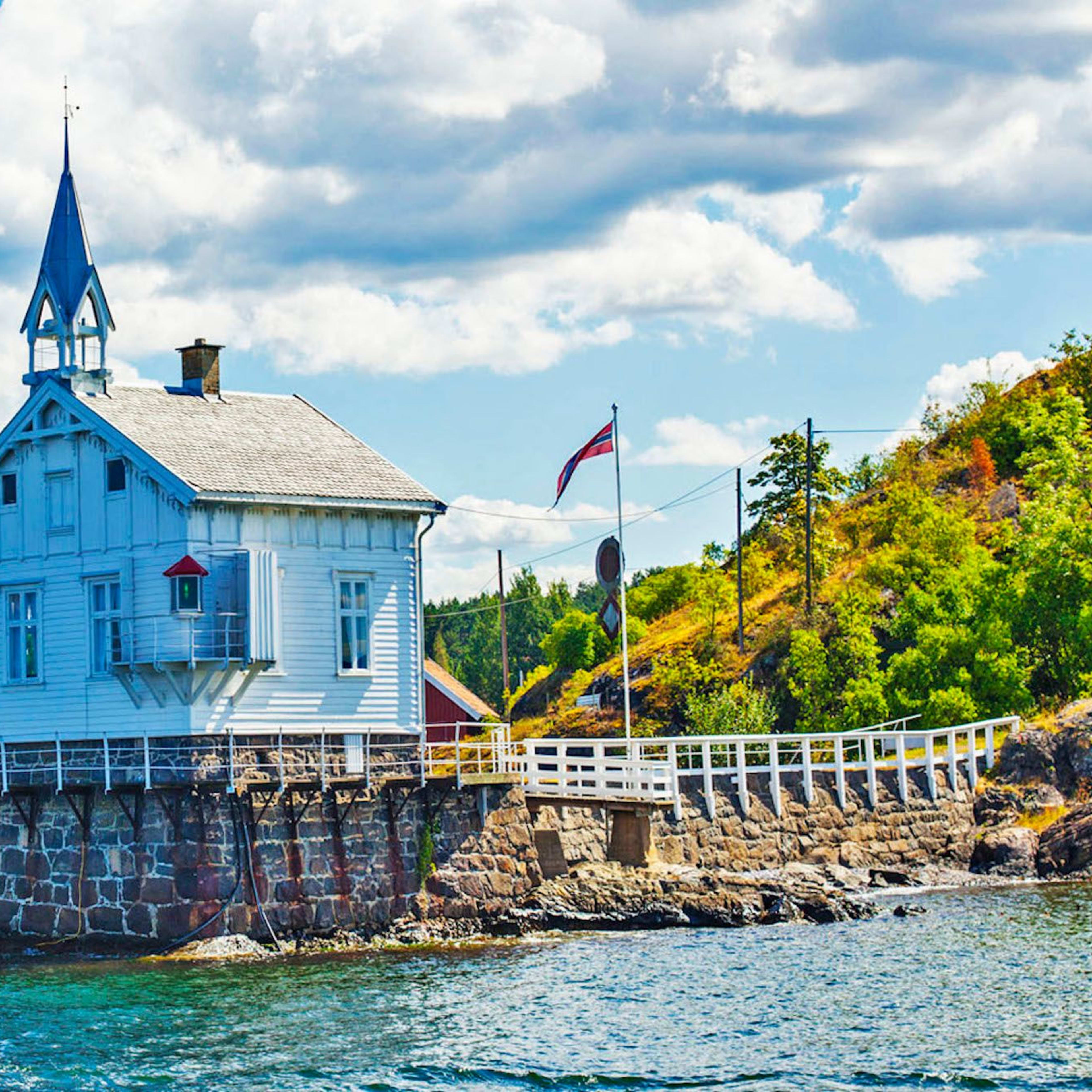 White wooden lighthouse by the water with flag and trees.