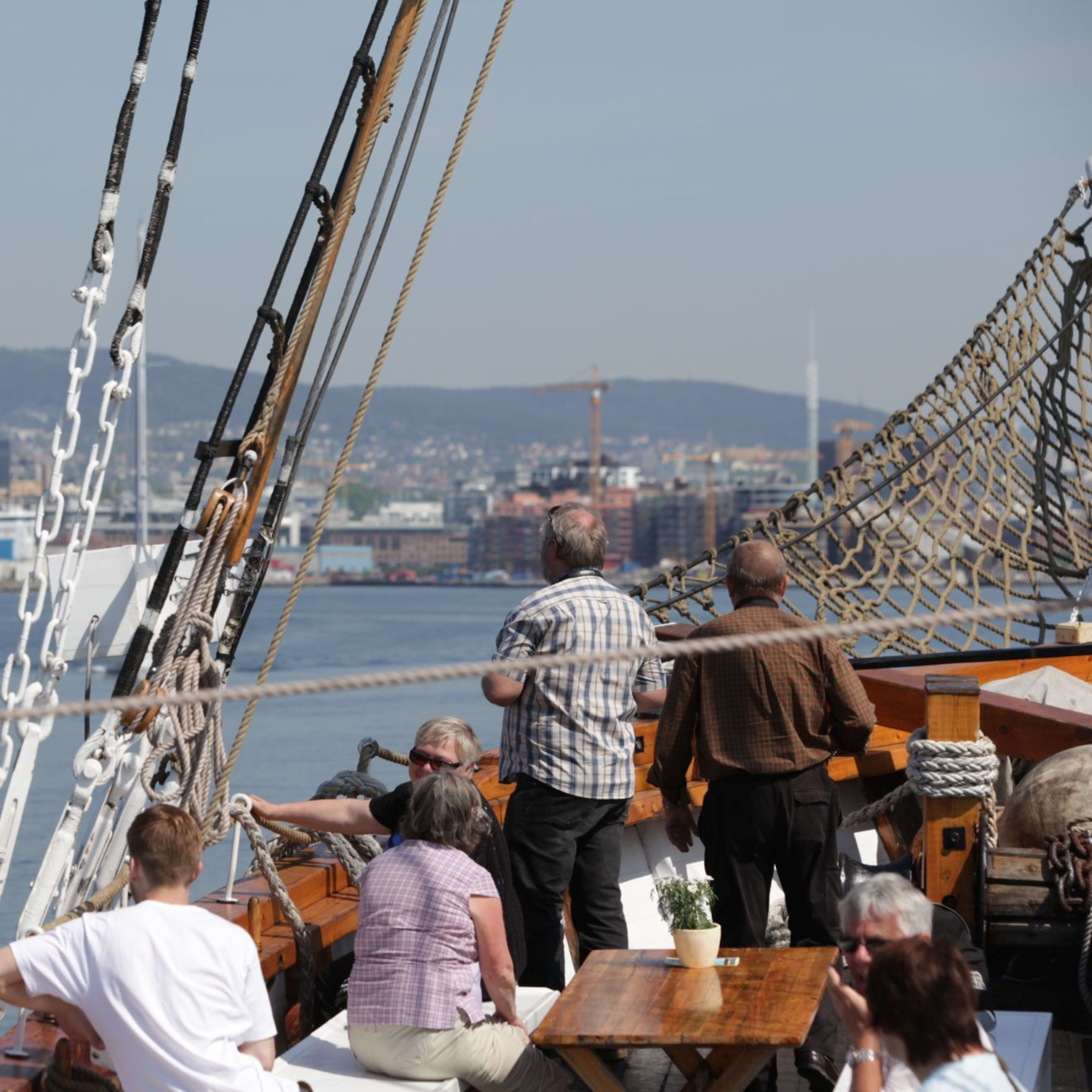 People relax on sailing ship deck approaching Oslo harbor.