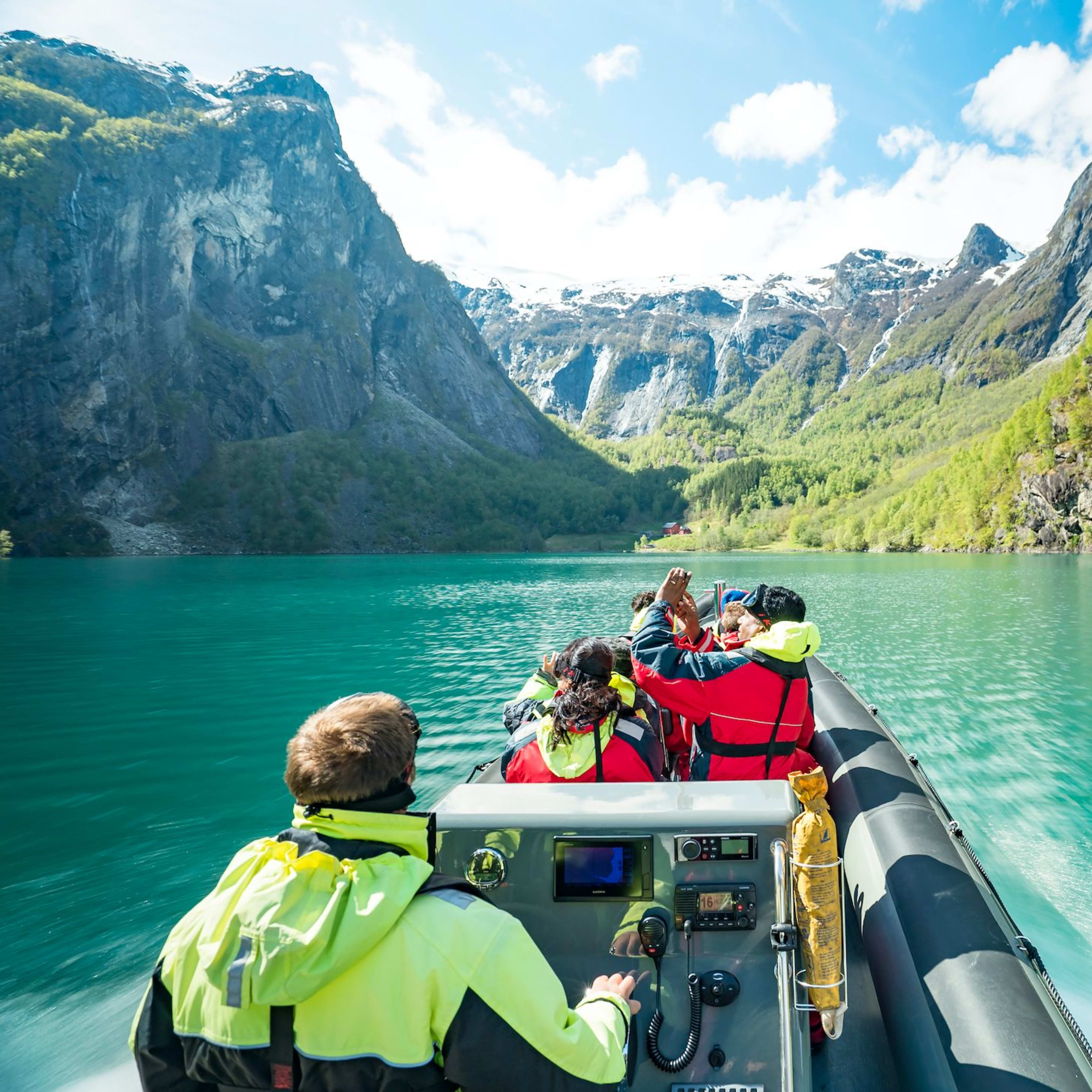 Tourists enjoying boat ride through turquoise Sognefjord Fjord surrounded by rocky cliffs