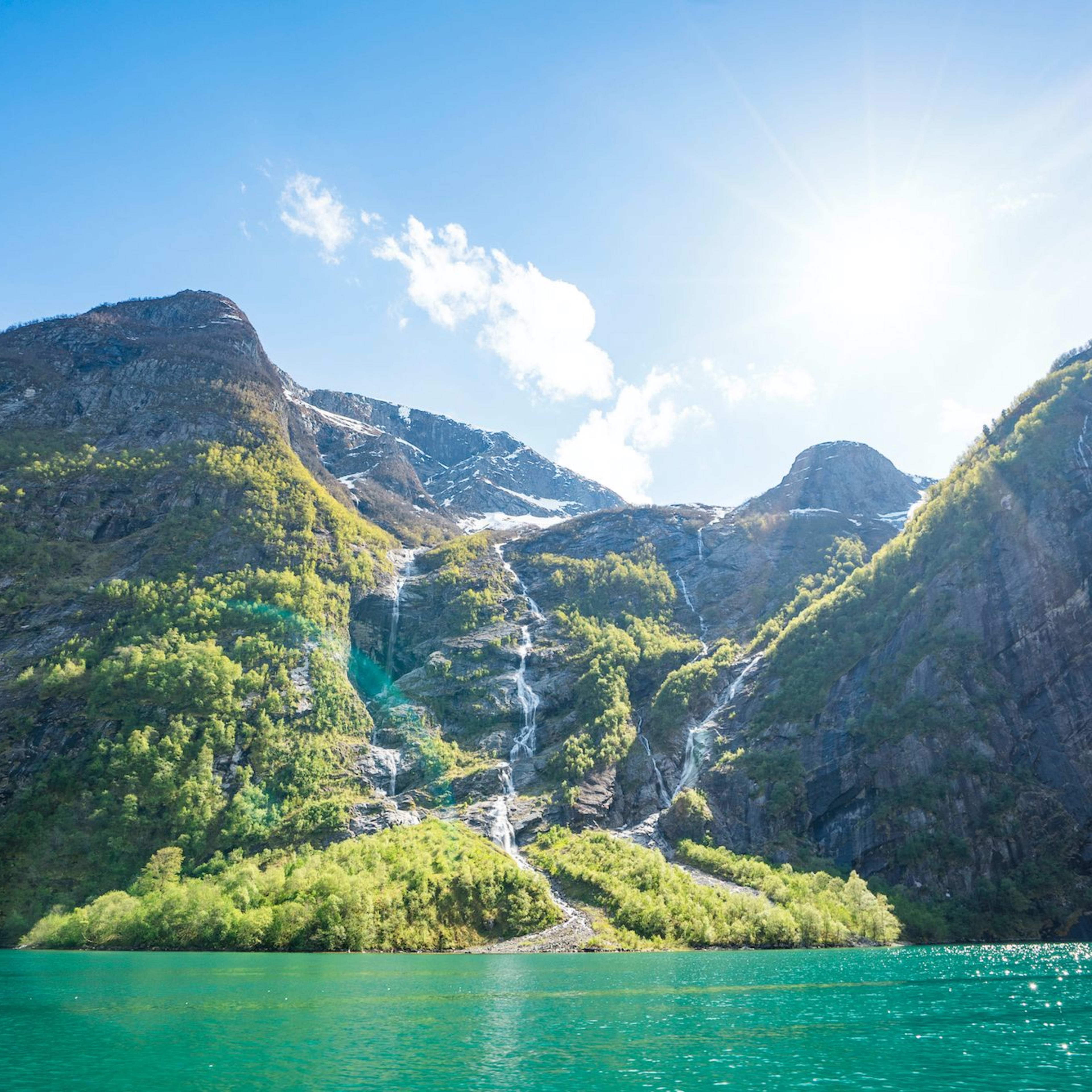 Turquoise Sognefjord with lush cliffs, waterfalls, and sunlight pouring over the landscape.