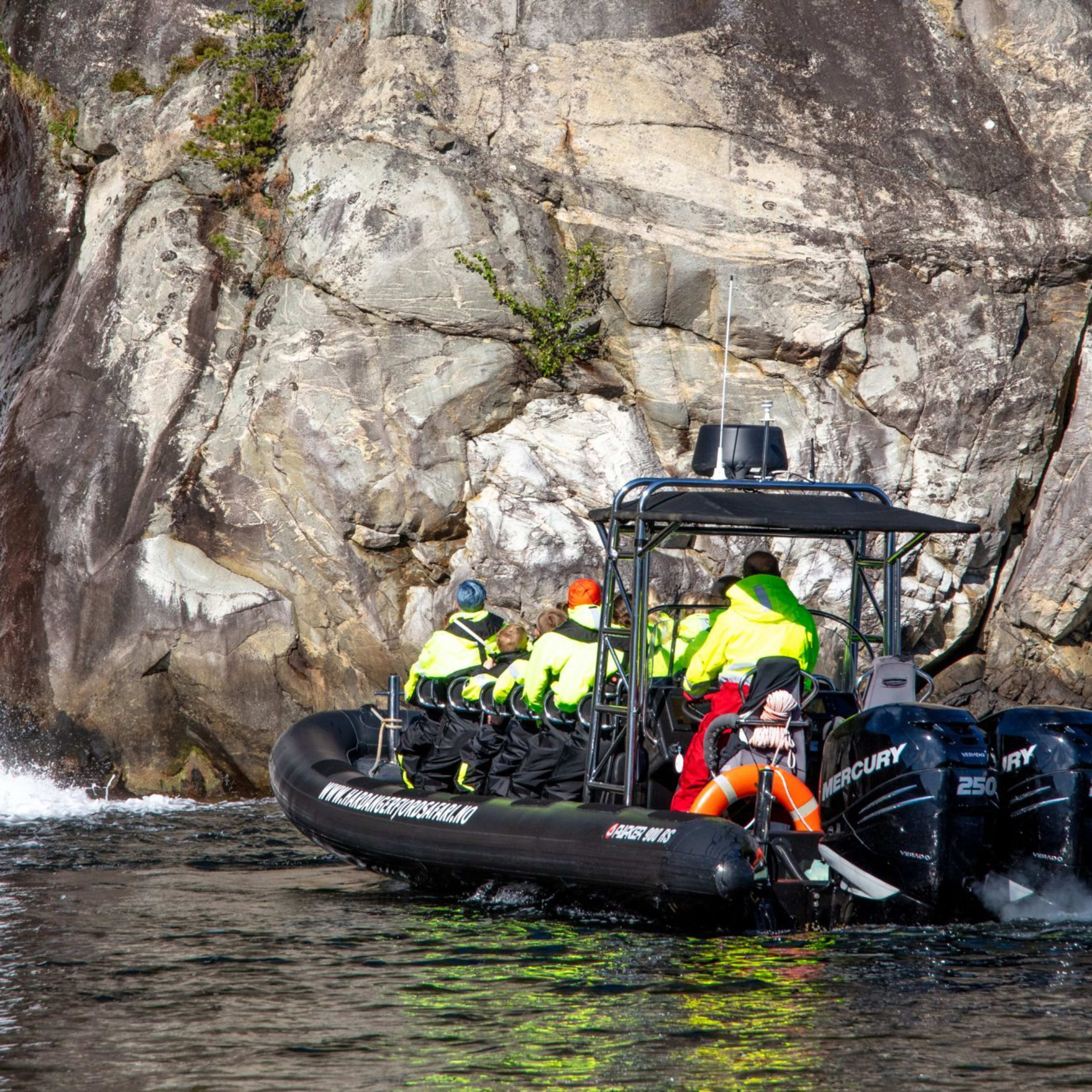 RIB boat nears cliffside waterfall with passengers in yellow.